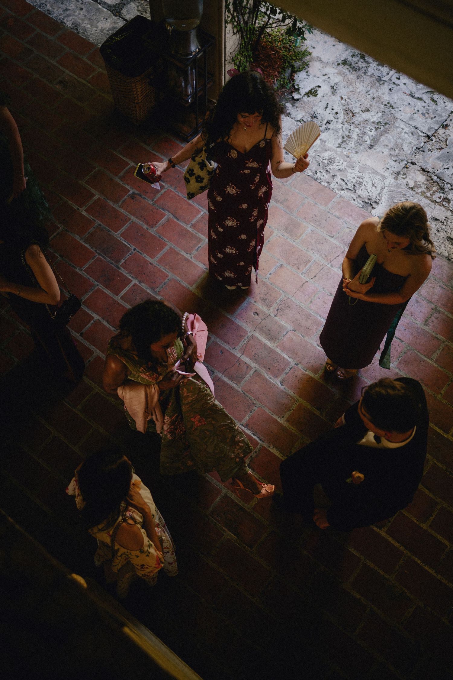 Aerial view of elegantly dressed guests socializing on a brick courtyard at an evening event.