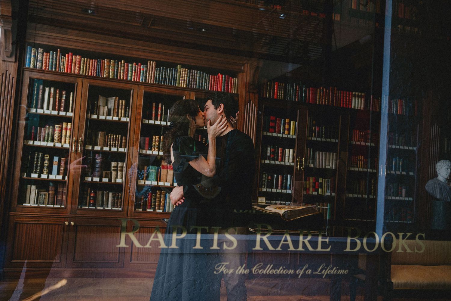 Couple sharing a romantic kiss in a classic library at Kaptis Kare Books, surrounded by shelves of antique books.