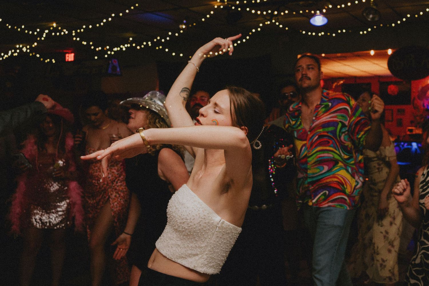 Woman dancing energetically at a lively party with colorful lights and festive crowd in the background.