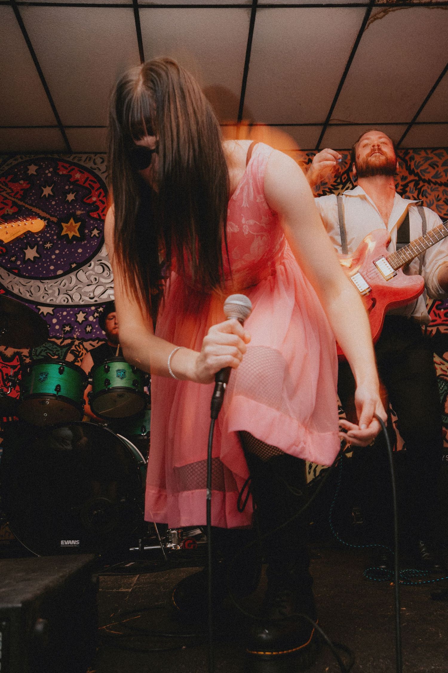Female vocalist in pink dress performs live on stage with guitarist and colorful psychedelic backdrop at a wedding.