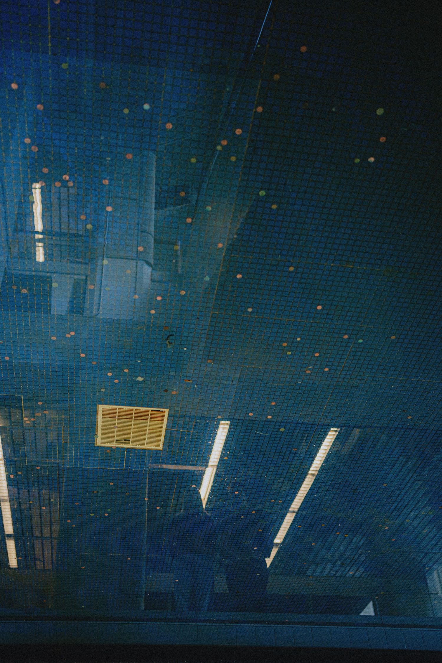 Blue-tinted industrial ceiling with glowing orange dots and fluorescent lights in a modern architectural interior.