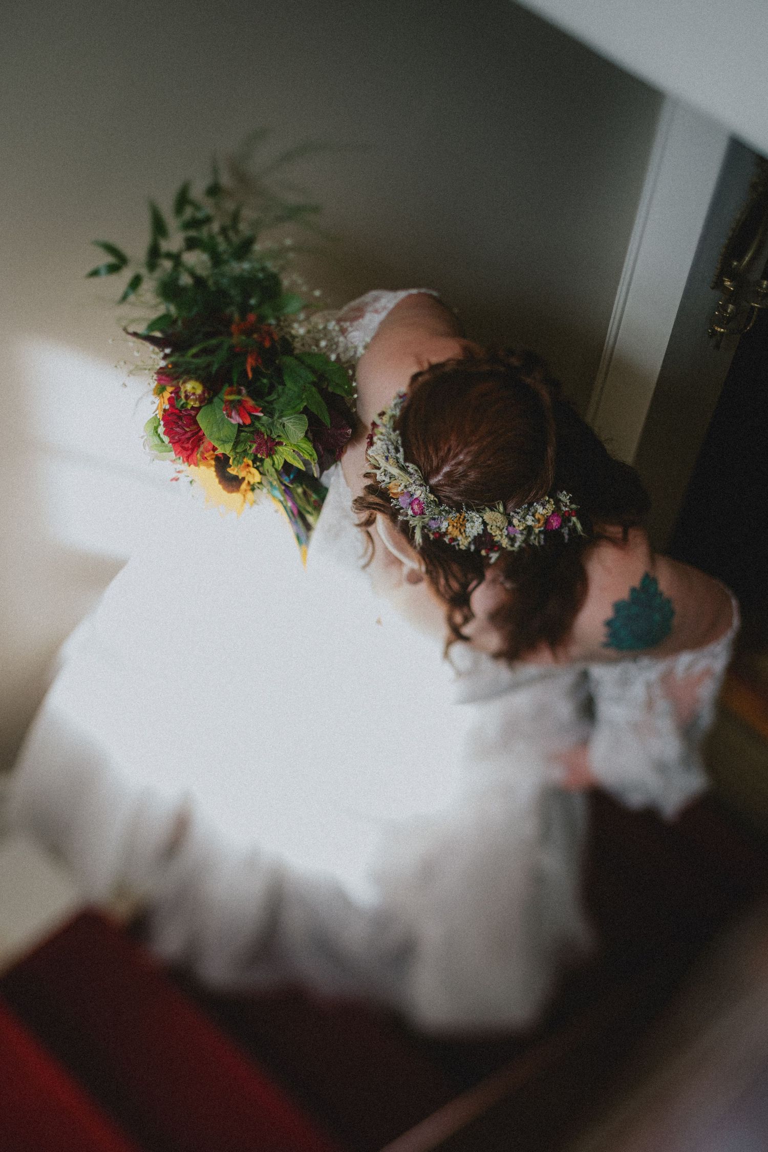 Bride in white dress with floral crown holds colorful bouquet, viewed from above on staircase.