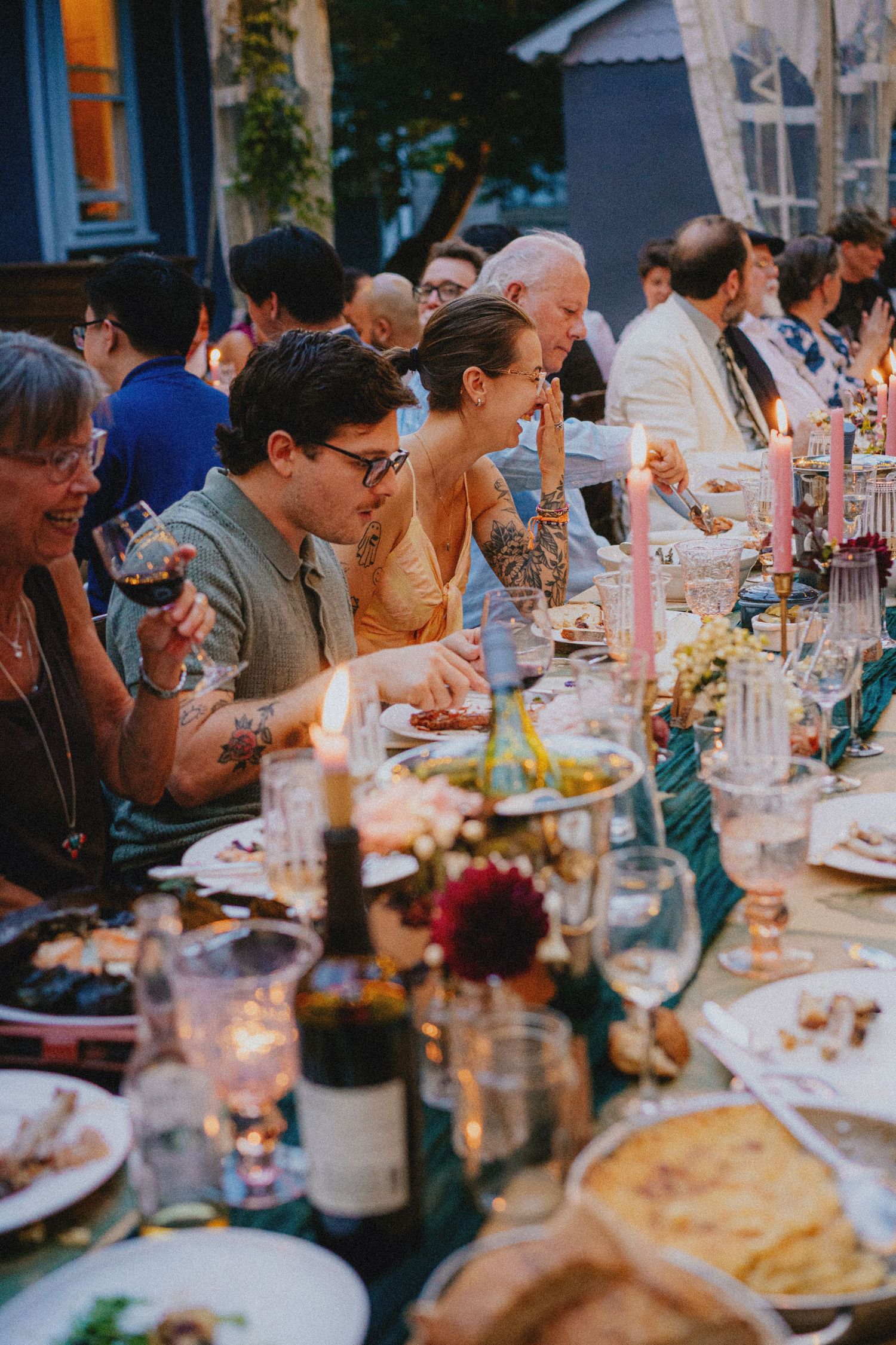 Guests gathered around a candlelit outdoor dinner table, enjoying wine and food at an elegant evening garden party.