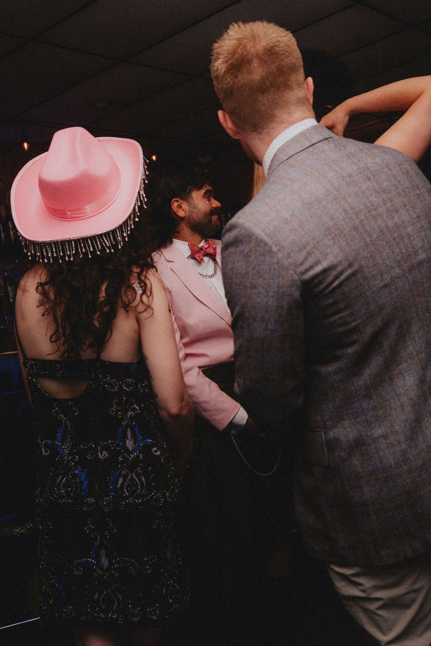 People dancing at a party, woman in pink cowboy hat and floral dress, man in pink suit with red bow tie.