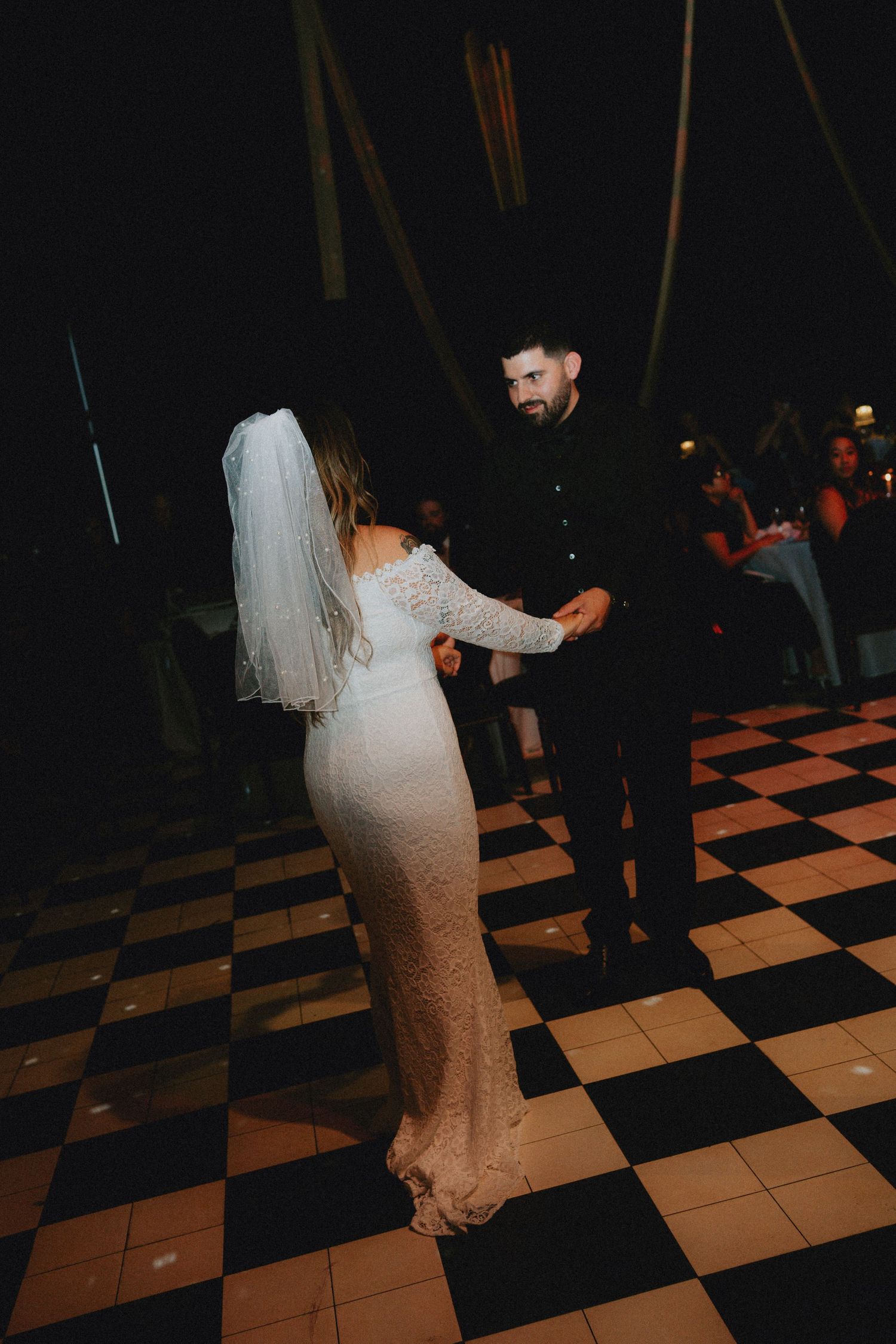 Bride and groom share their first dance on a checkered black and white dance floor at a romantic evening wedding reception.