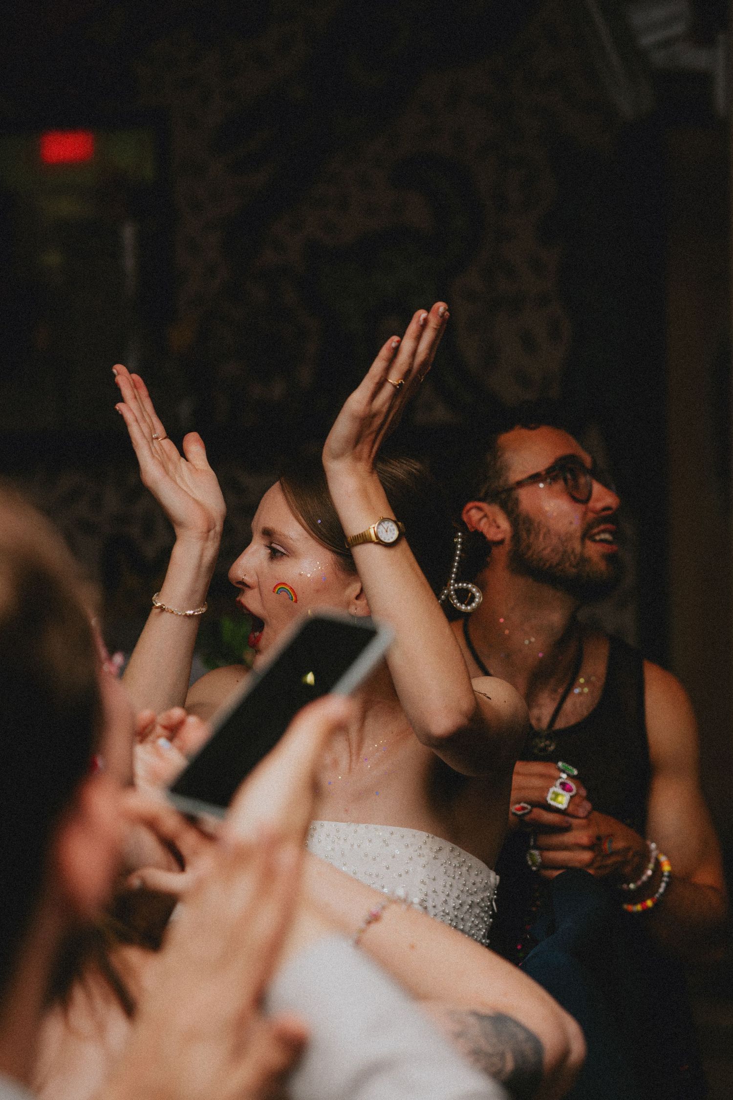 A bride with hands raised dancing joyfully beside a man at a lively wedding reception party.