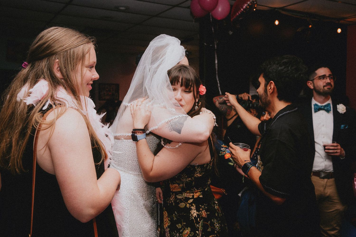 Bride in white gown and veil shares a warm hug with a guest on the wedding reception dance floor.