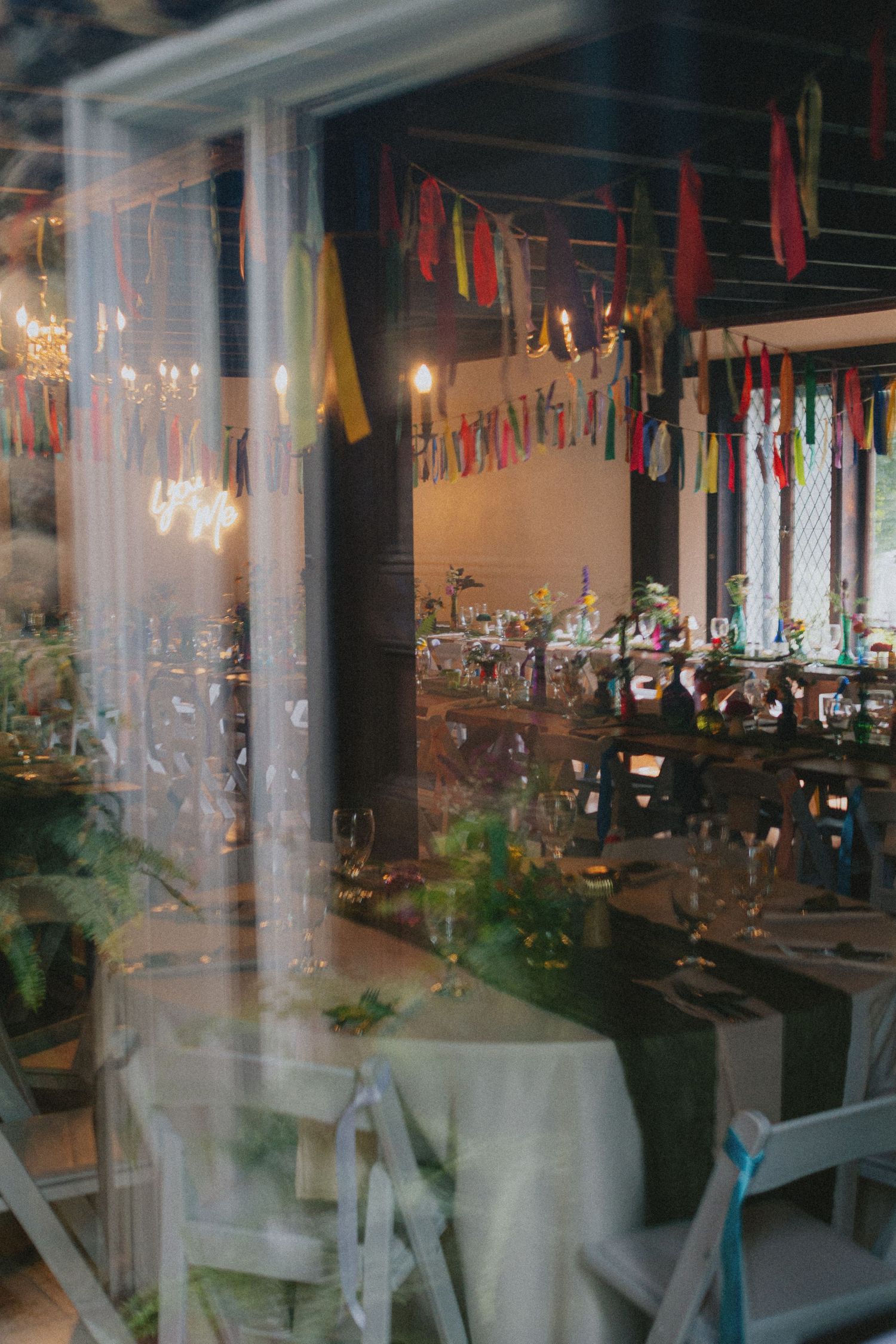 Colorful bunting decorates a festive indoor event venue with candlelit tables set for a celebration.