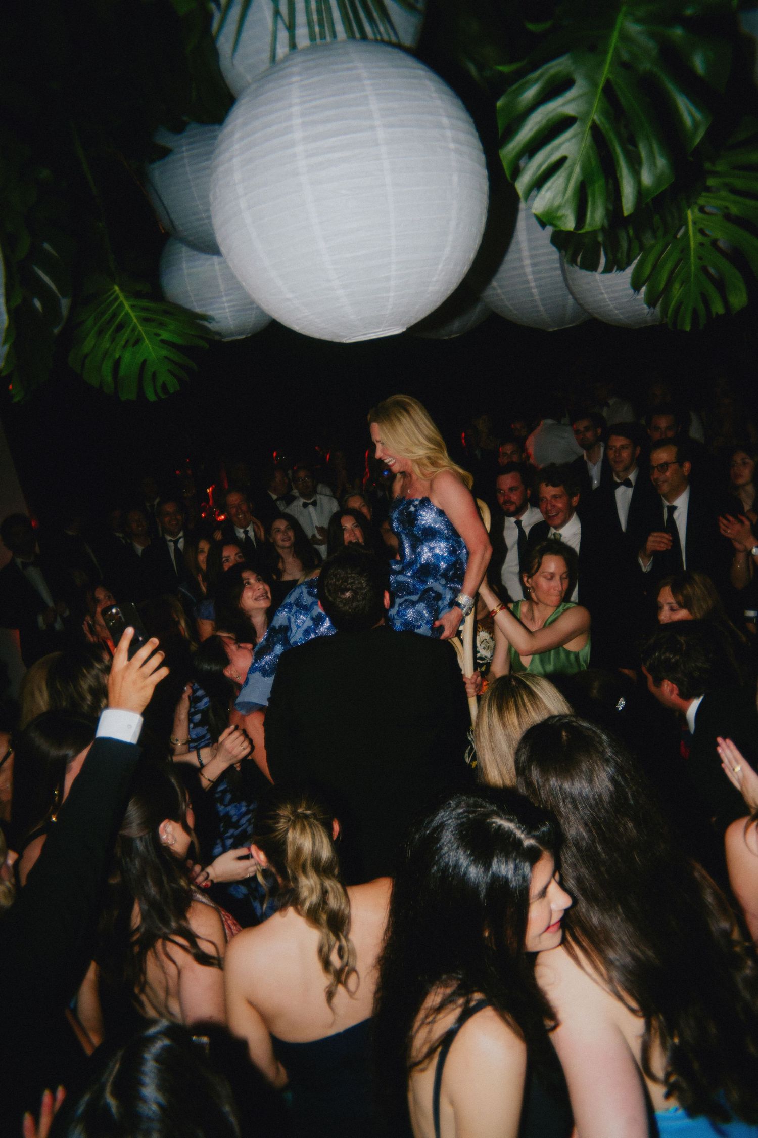 Guests dancing at an elegant wedding reception with white paper lantern decorations and tropical greenery.