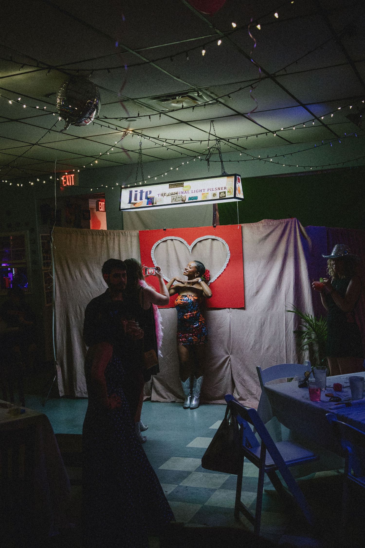 Performer in colorful dress sings on stage before heart backdrop at dimly lit venue with string lights.