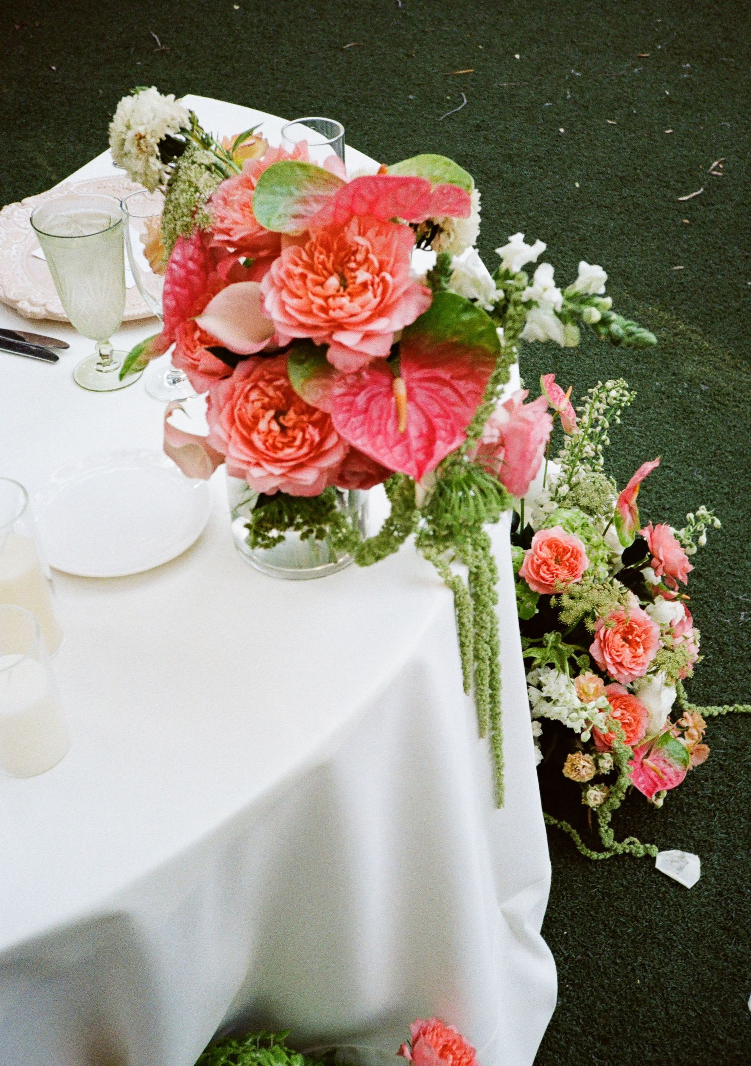 Elegant wedding table with white linen and lush pink coral floral centerpiece featuring roses and anthuriums.