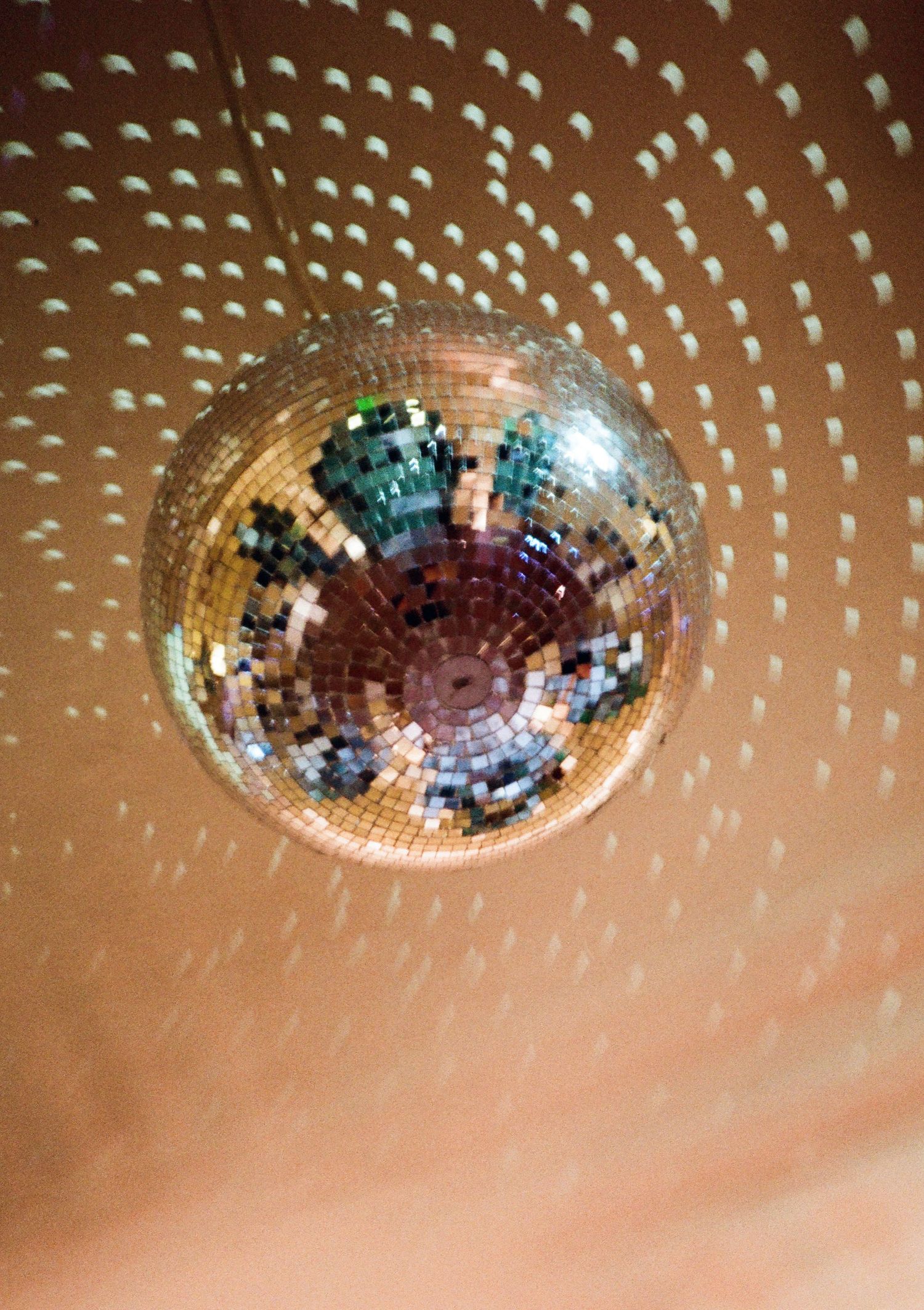 A shimmering disco ball hanging from the ceiling, casting circular light patterns on a warm orange surface.