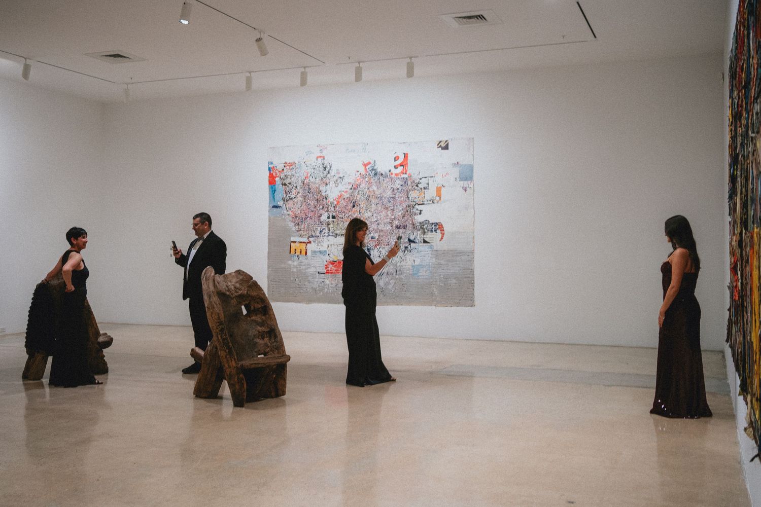Elegantly dressed gallery staff in black gowns stand near modern artwork in a bright contemporary art gallery.