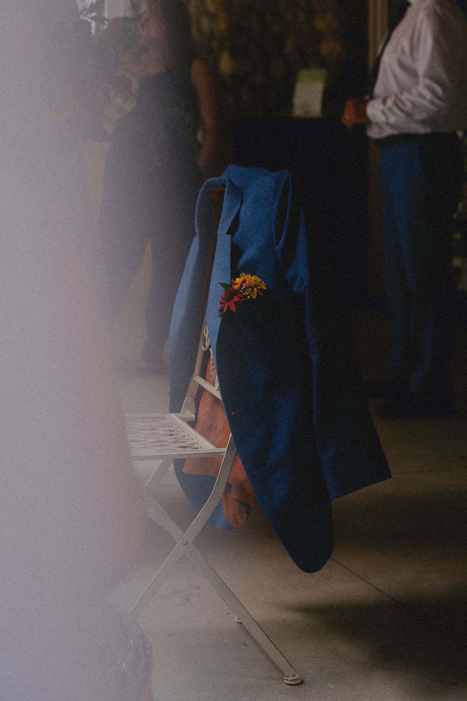 Blue tote bag with colorful flowers in pocket resting on white folding chair at an indoor event.