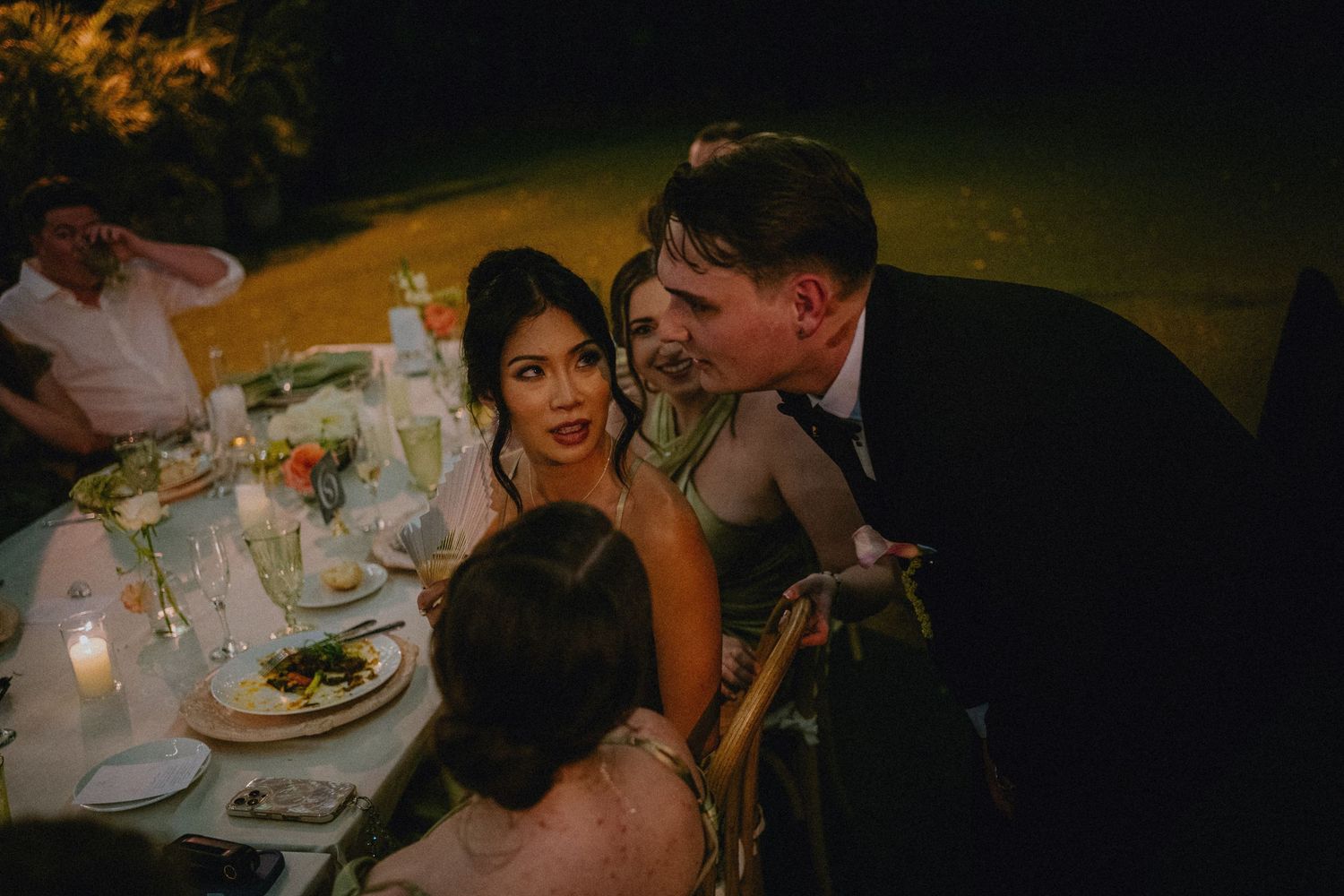 Couple sharing an intimate moment at a candlelit outdoor wedding reception dinner table at night.