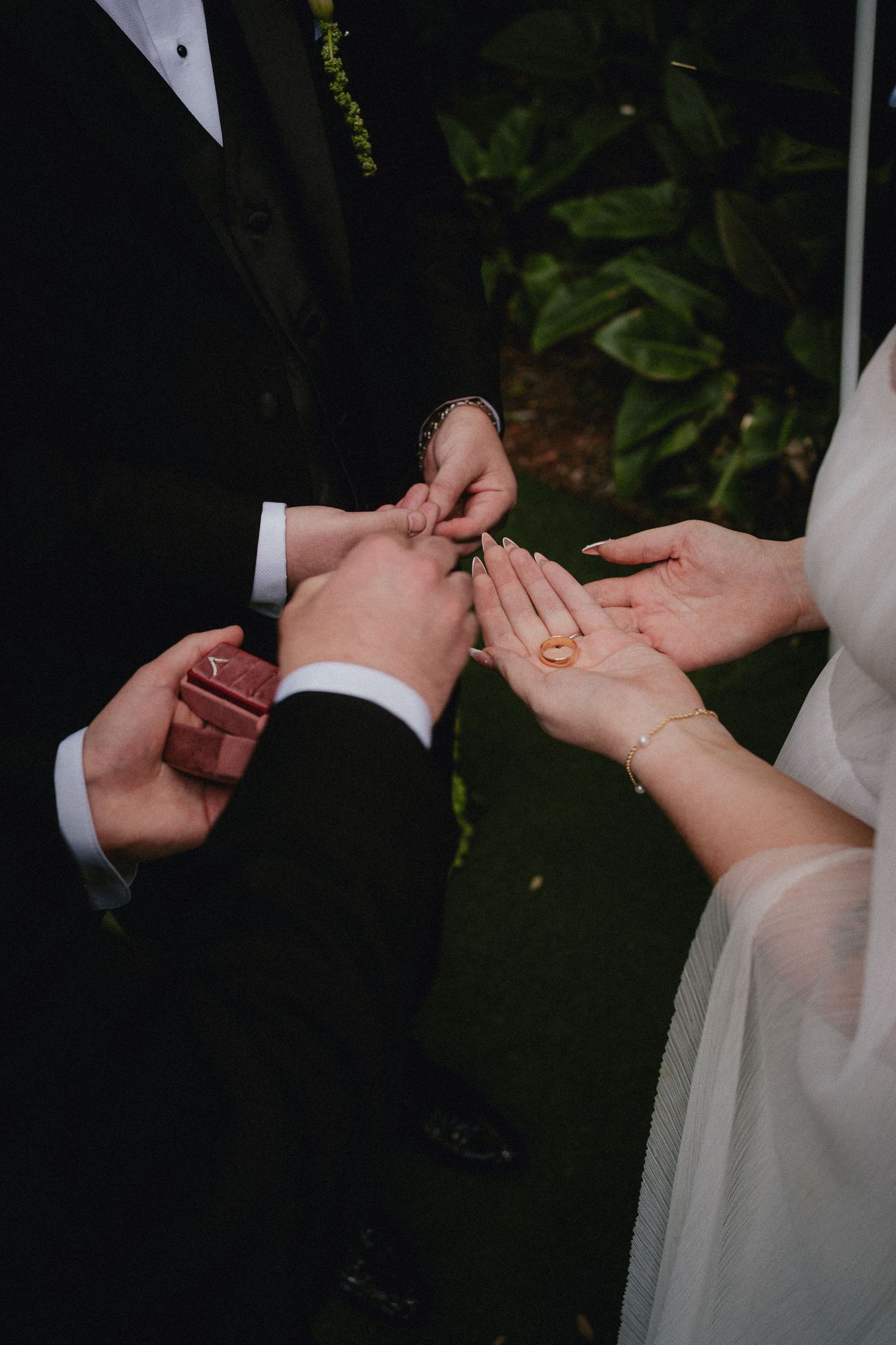 Close-up of wedding ring exchange ceremony, bride holding gold band on outstretched palm during outdoor nuptials.