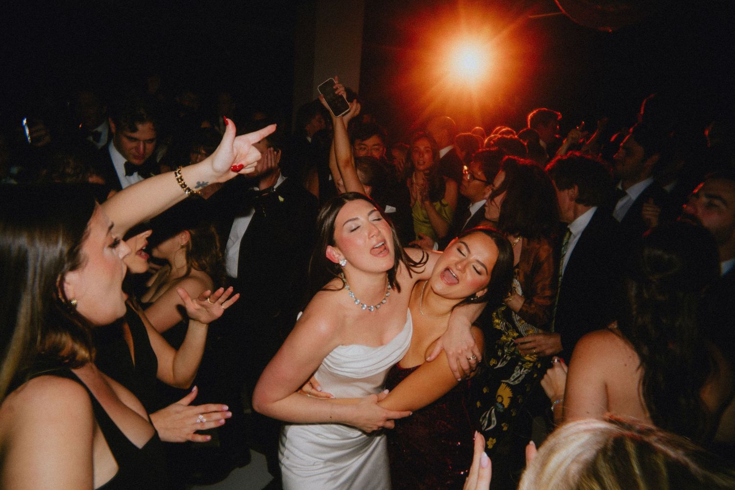 Bride in white dress dancing joyfully with friends at a lively wedding reception party.