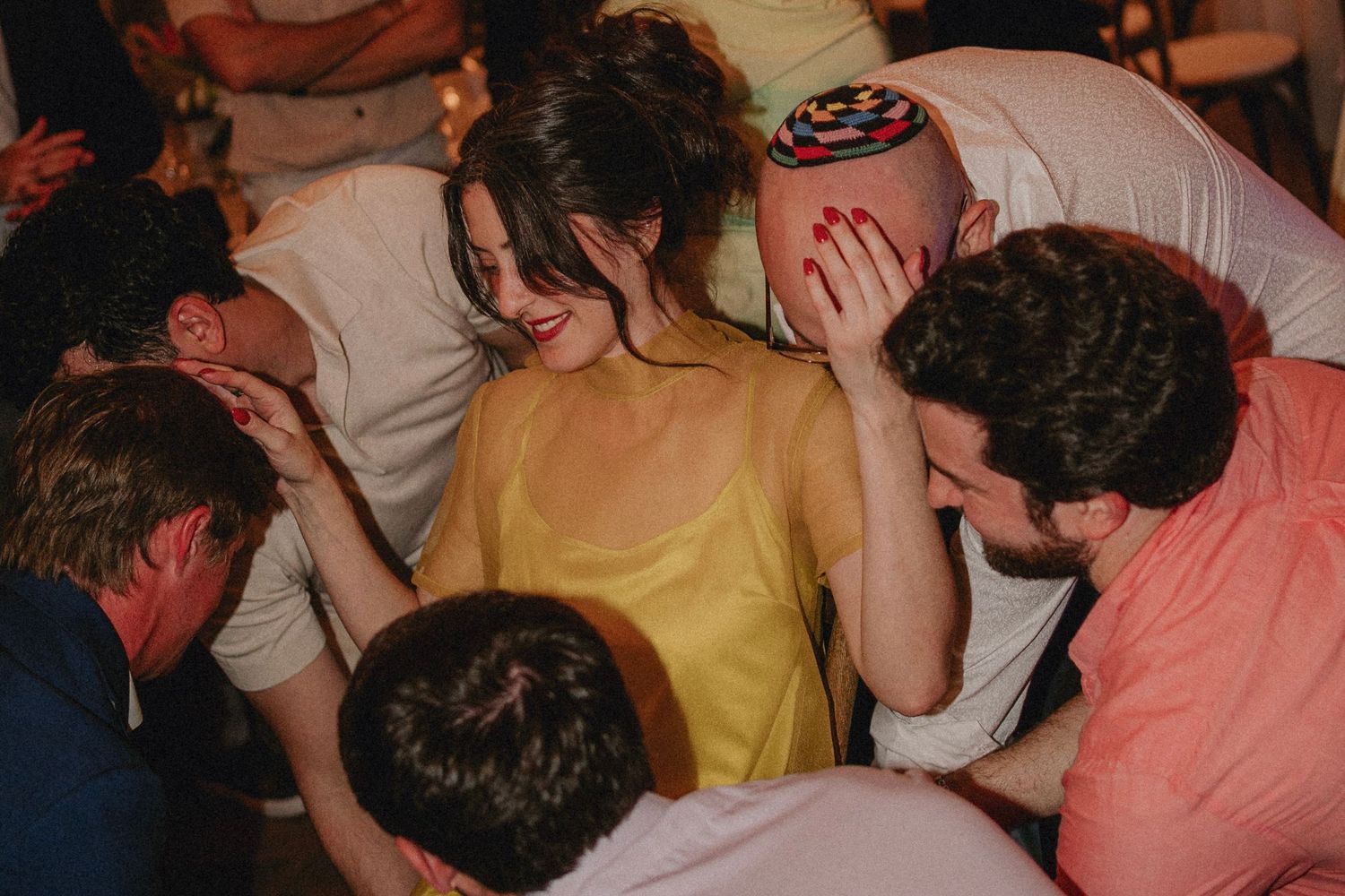 Woman in yellow dress smiling surrounded by friends at a lively wedding reception party celebration.
