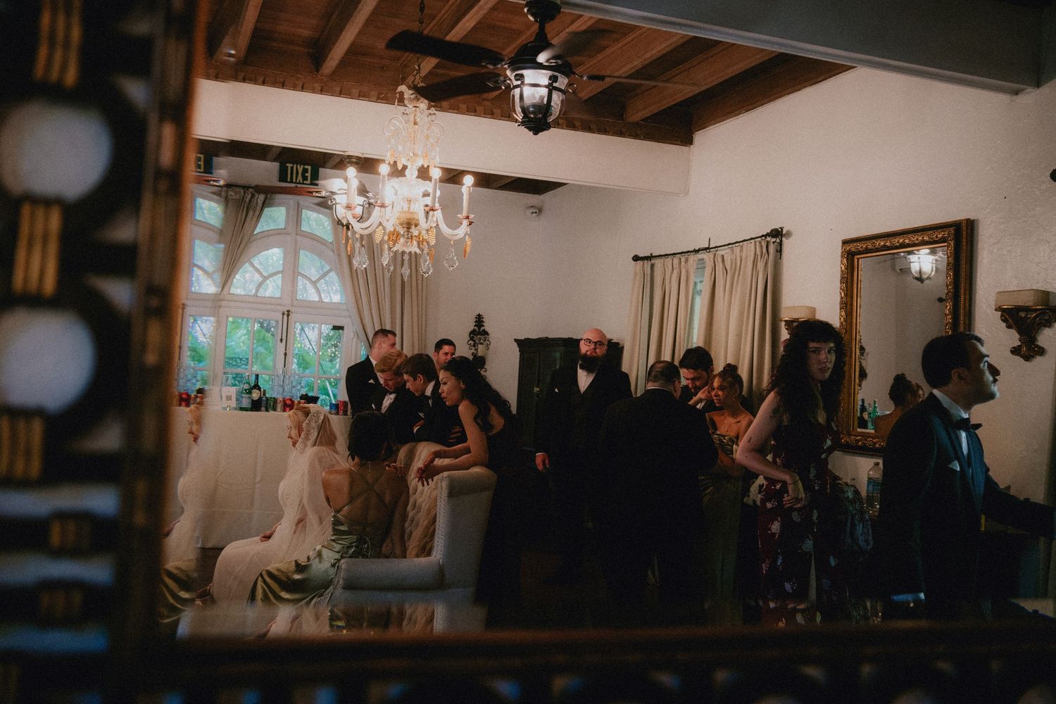 Elegant wedding reception in a rustic venue with chandelier lighting, guests mingling, and a bride in white gown.