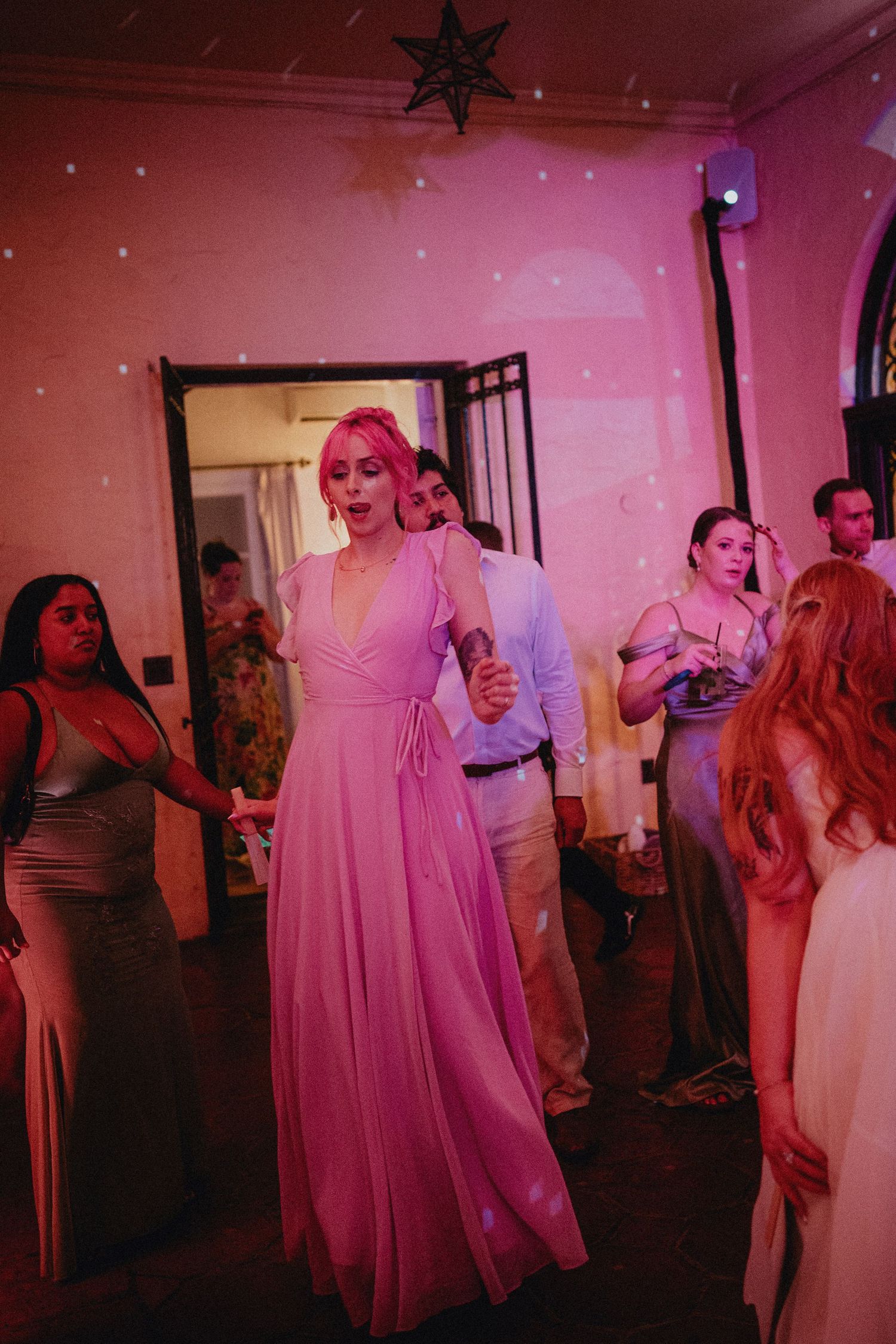 Woman in pink maxi dress dancing at a wedding reception under pink lights and star decorations.