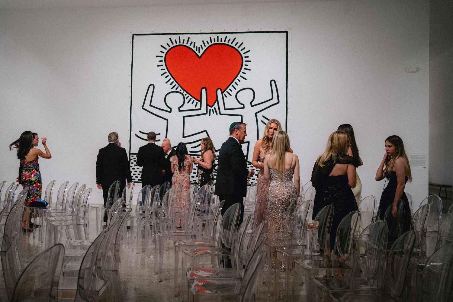 Elegantly dressed guests mingle at an upscale event beneath a bold Keith Haring heart mural.