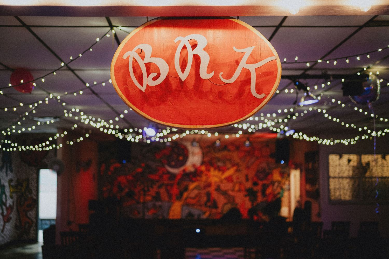 BRK neon sign glowing red above string lights in a dimly lit bar with colorful mural backdrop.
