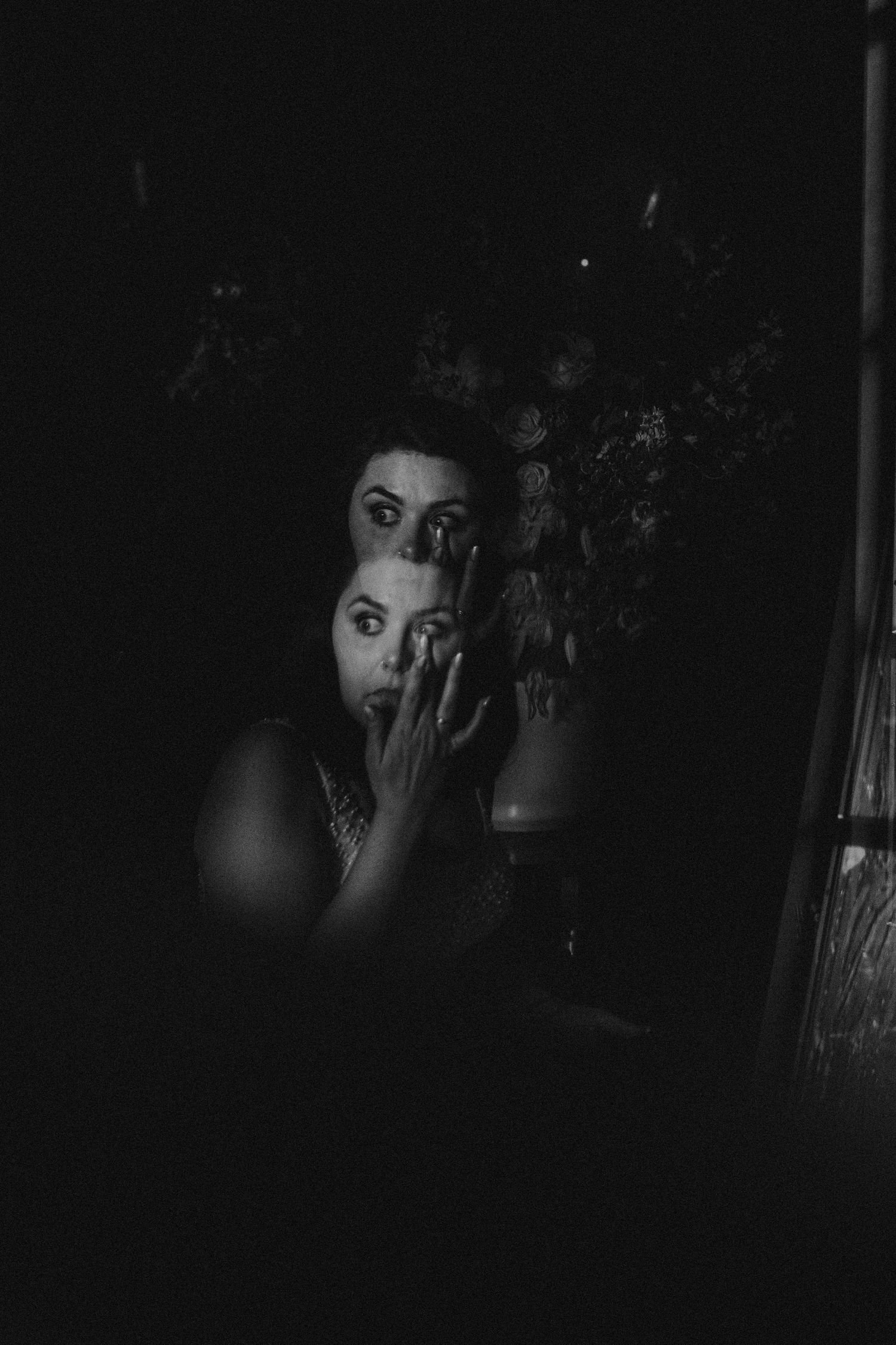 Dark moody black and white portrait of a woman holding her hand to her face near a vase of flowers.
