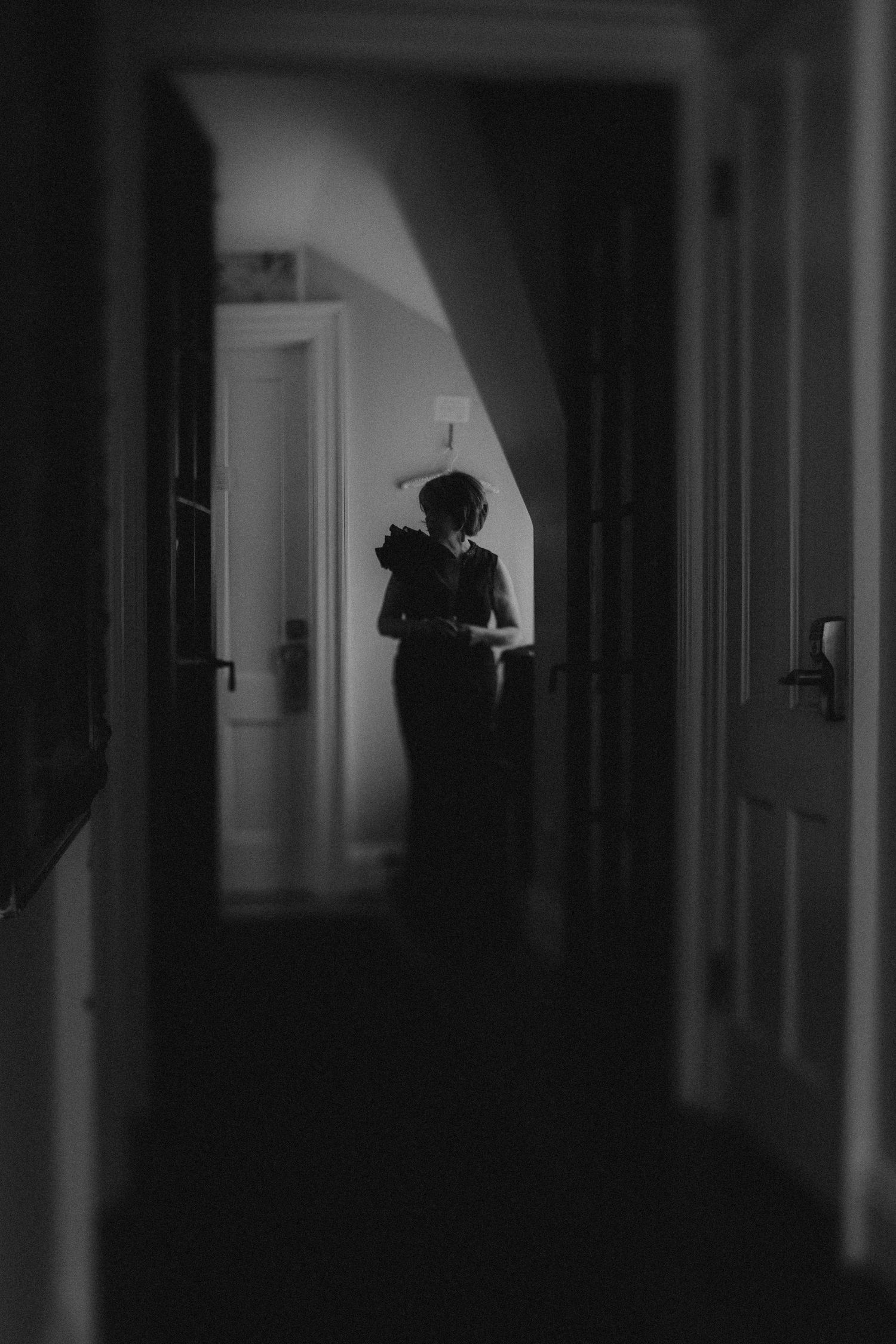 Silhouette of a person standing in a dimly lit hallway, captured in moody black and white photography.