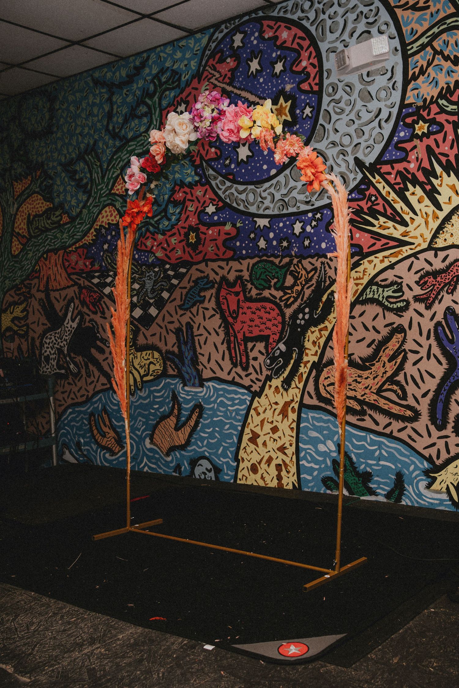 Gold arch with colorful floral crown display in front of vibrant psychedelic mural wall art backdrop.