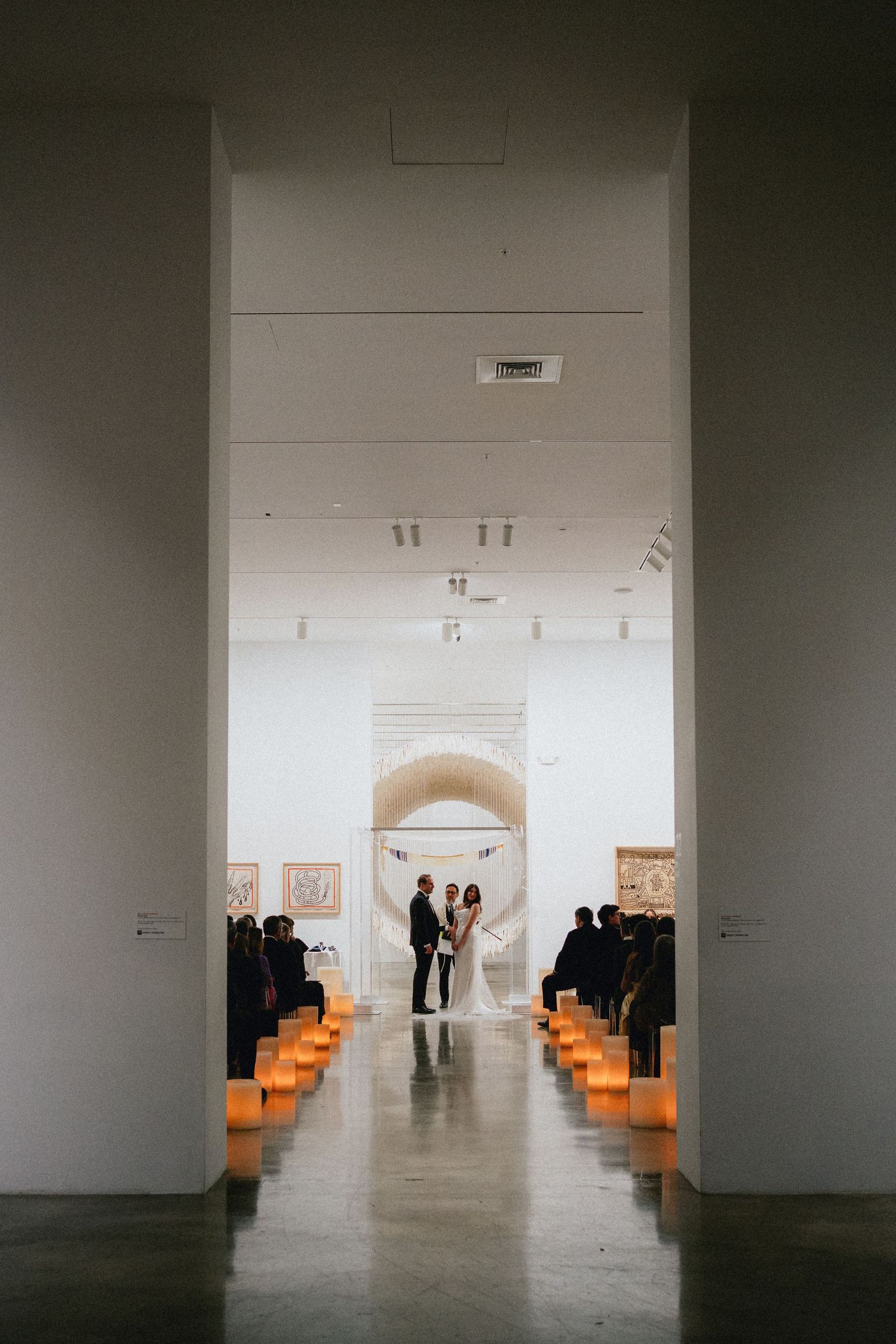 Elegant wedding ceremony in a modern art gallery with candlelit aisle and couple standing at the altar.
