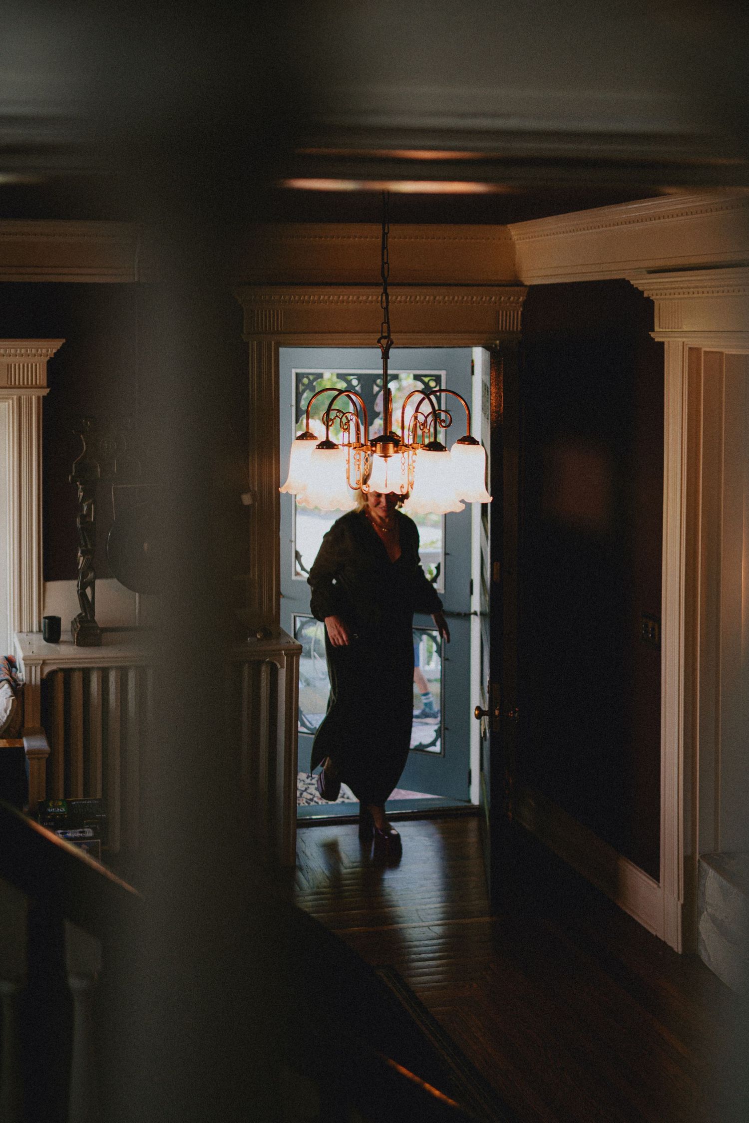 Person silhouetted in doorway of elegant home with chandelier and hardwood floors.