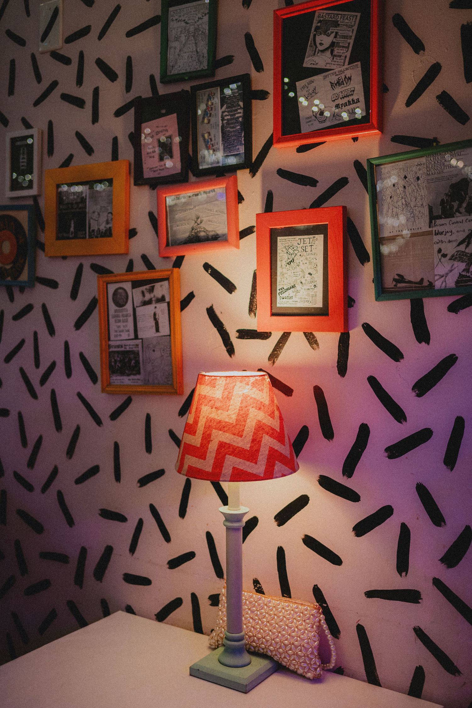 Colorful framed pictures on patterned wall with a glowing chevron lamp on a white desk.