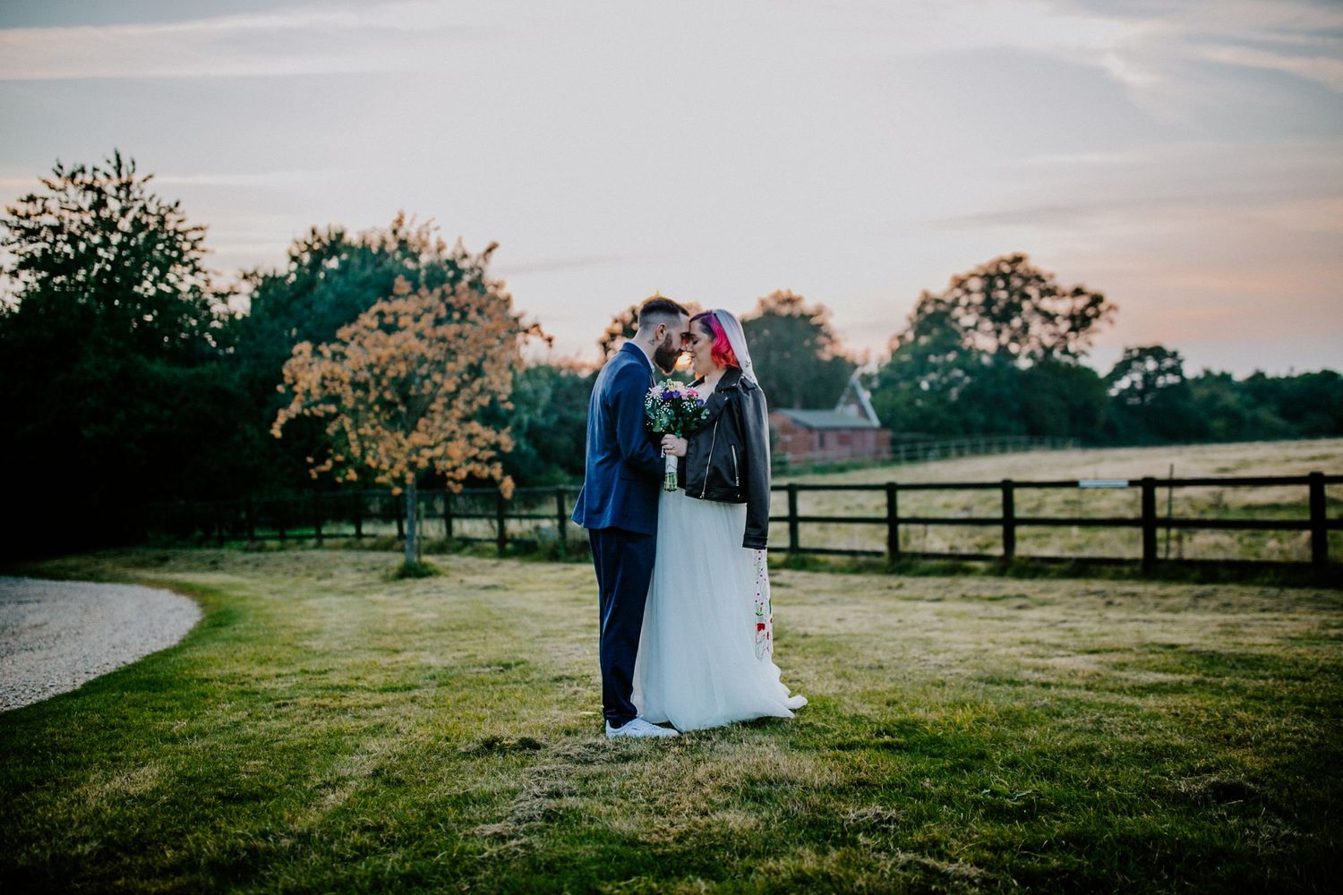 Golden hour magic – The bride and groom share a quiet moment in the fields of Lodge Farm House, the sunset casting a golden glow over them.
