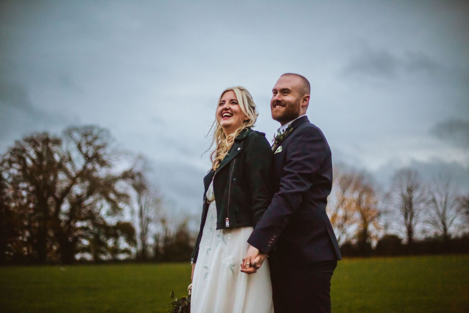 Bride and Groom posing outside Cottered Village Hall on a field  Hertfordshire, Photographer RELM Photography