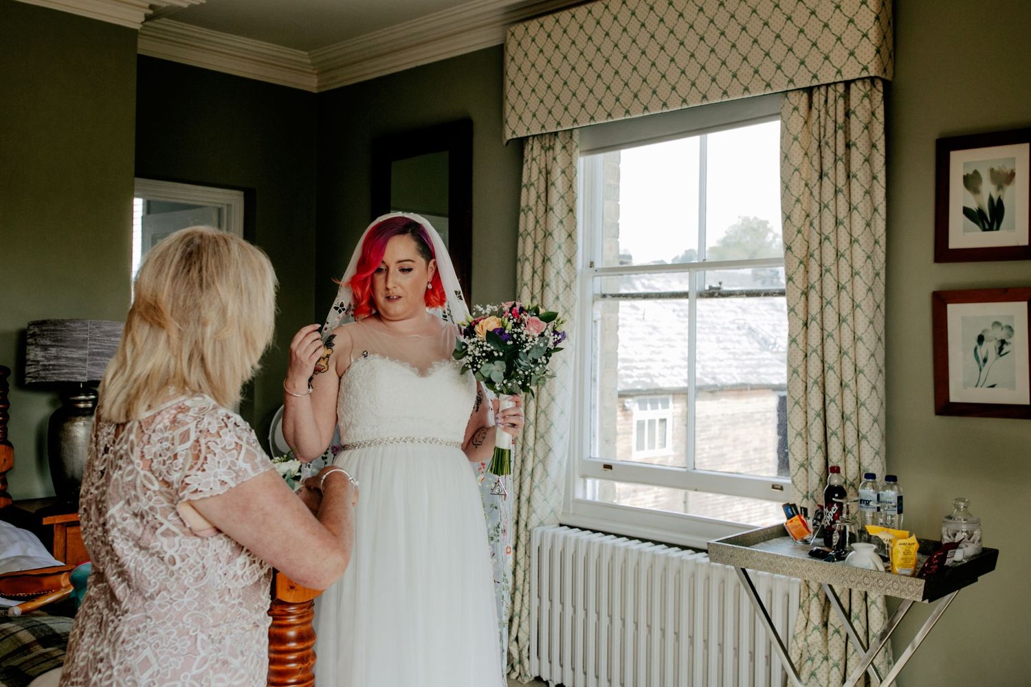 Final touches – The mother of the bride does final checks for her daughter, her vibrant pink hair making her bridal look truly unique.