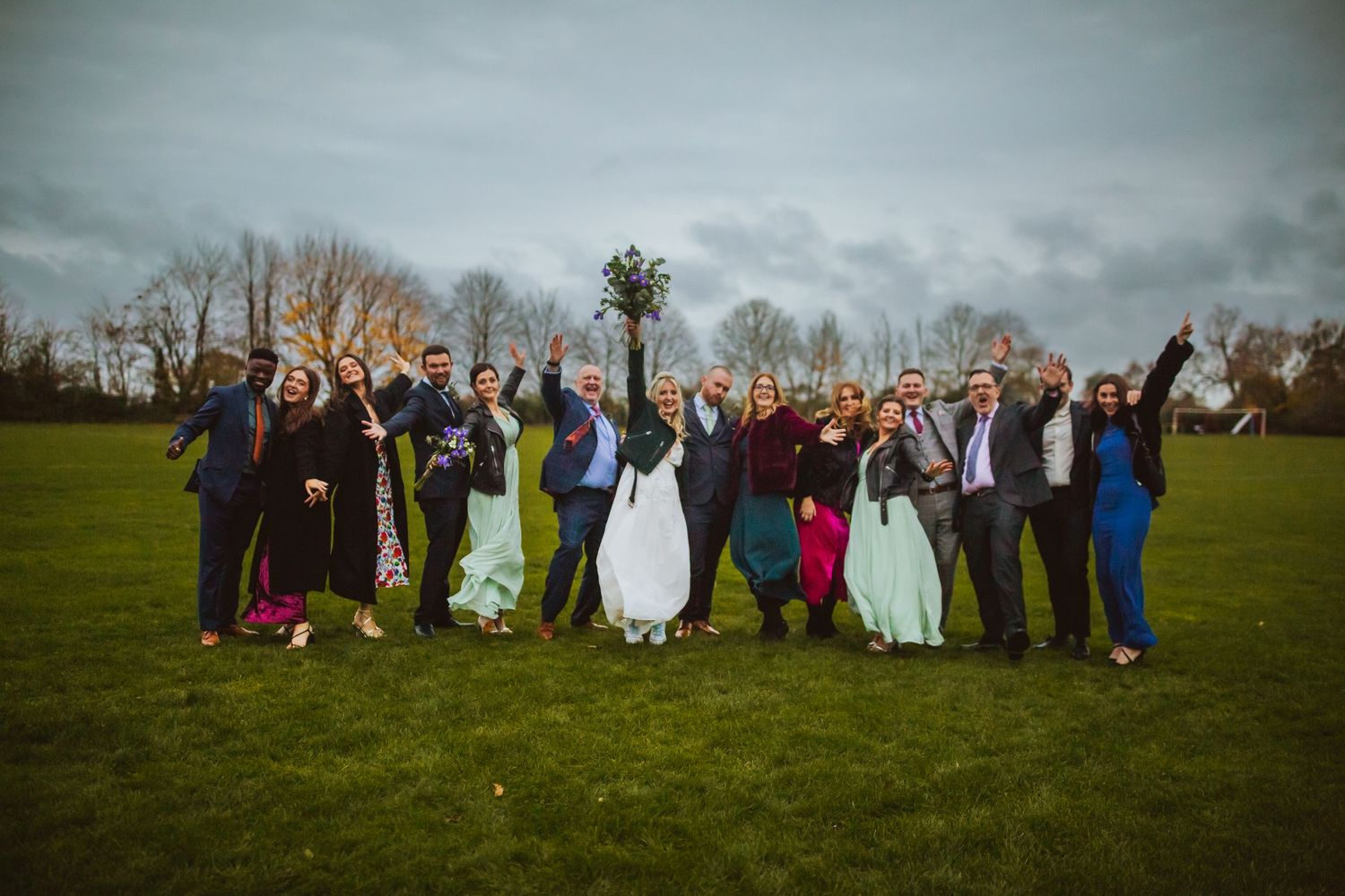 Bride and Grooms family fun pose outside Cottered Village Hall on a field  Hertfordshire, Photographer RELM Photography