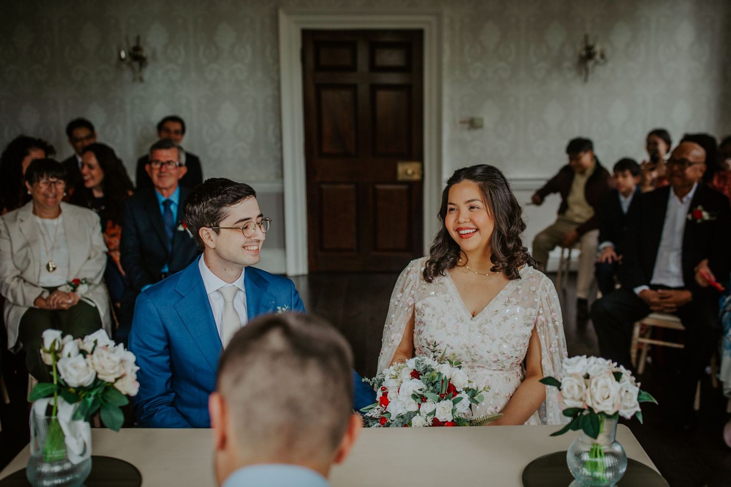 Bride and groom sit together beneath floral decorations during their wedding service at Morden Park.