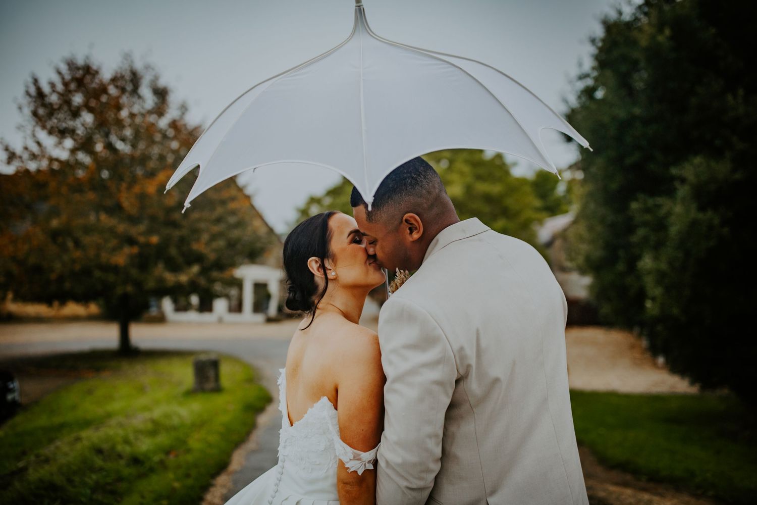 Bride and groom kissing under a white umbrella outside their wedding venue Lapstone Barn – Chipping Campden, The Cotswolds
