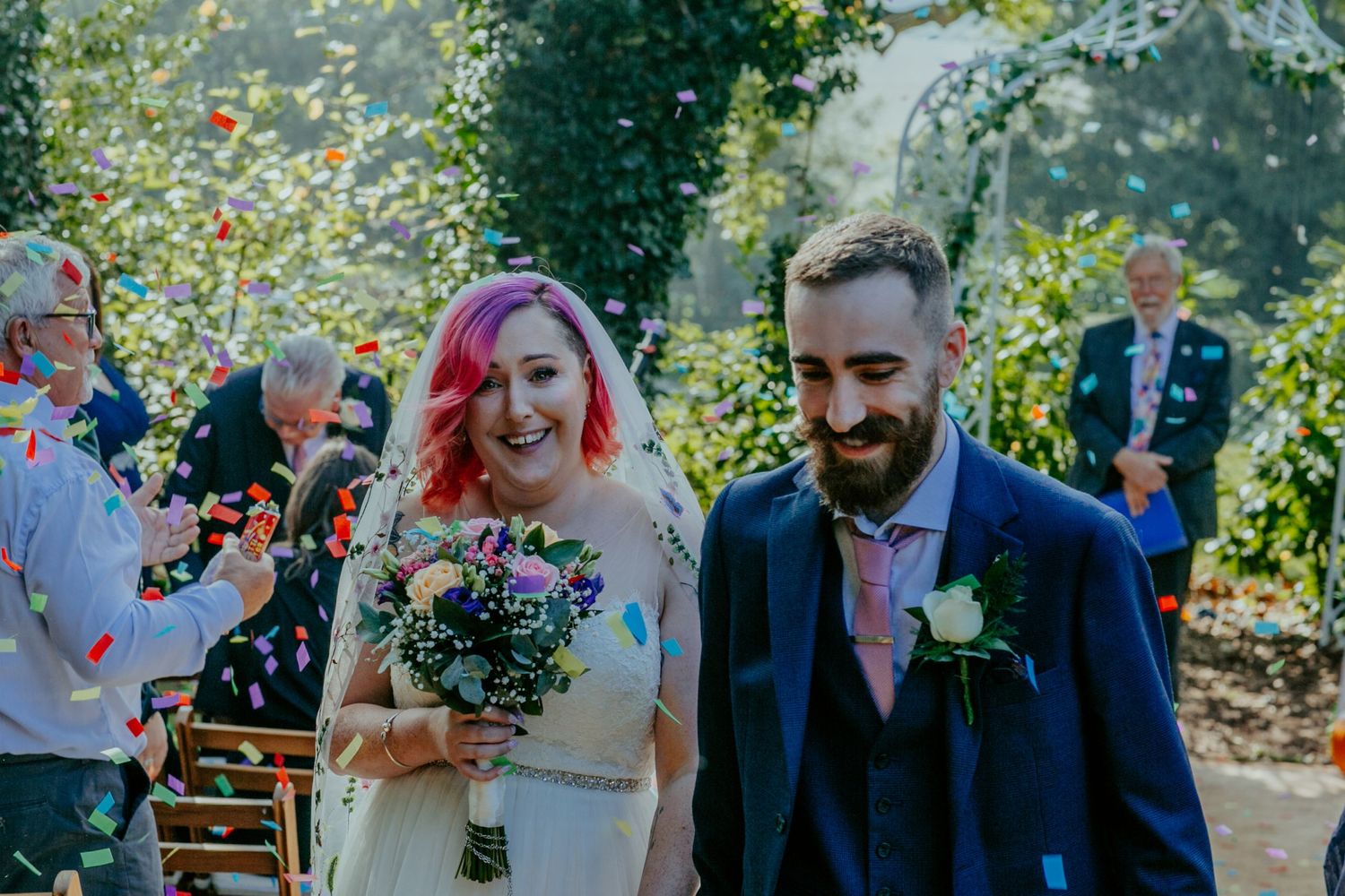 A burst of colour – The bride and groom laugh joyfully as a confetti cannon showers them in a rainbow of petals.