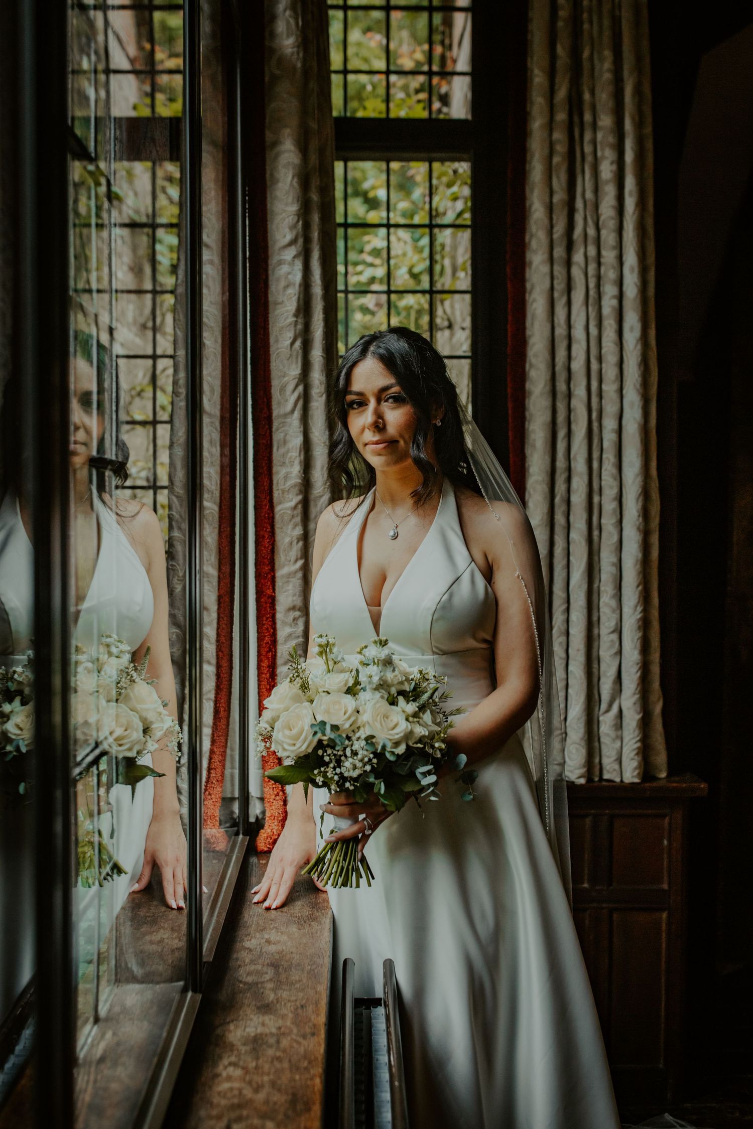 Bride standing by window at Ramster Hall, Chiddingfold, Godalming.