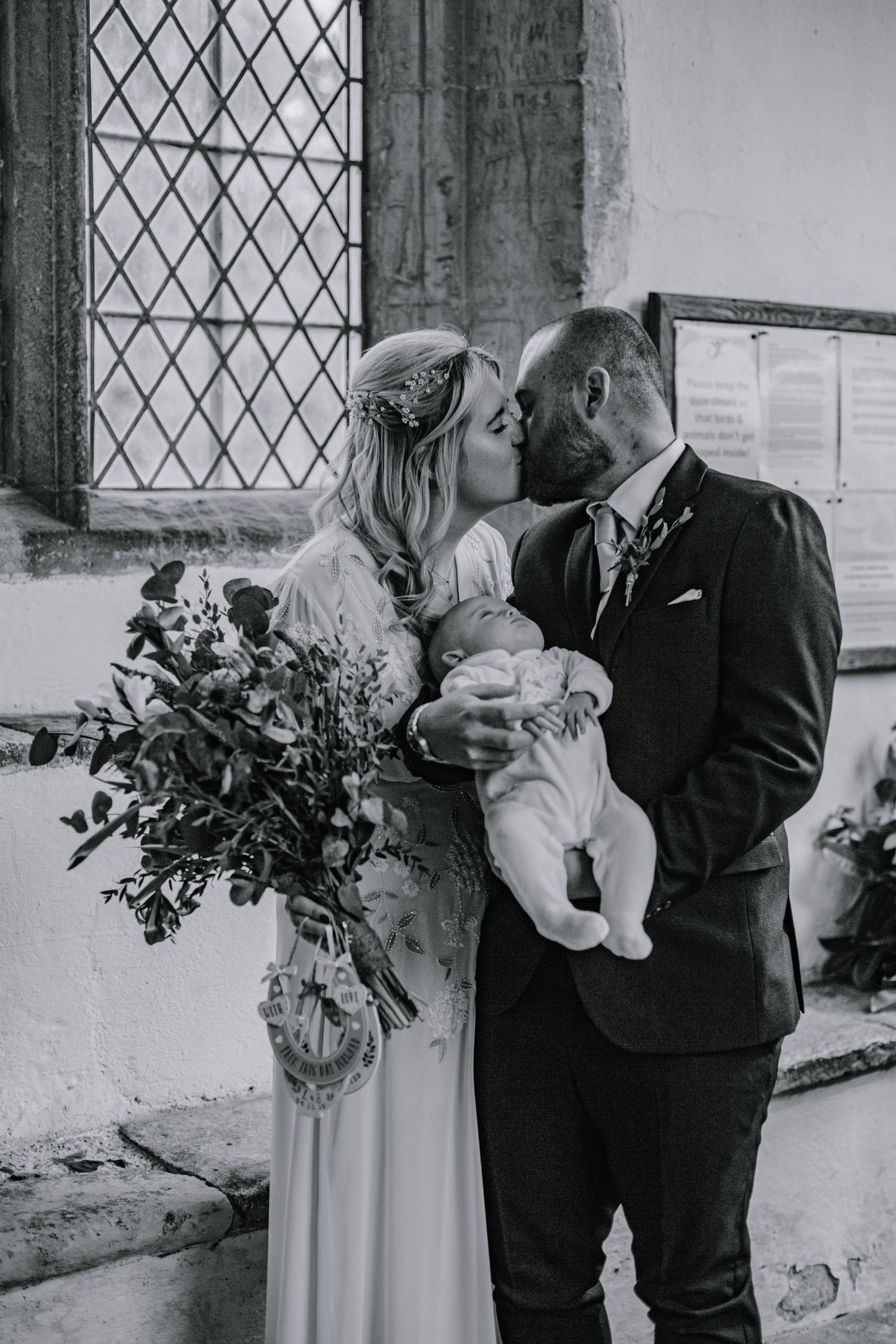 Bride and groom posing with newborn son at Braughing Church, Hertfordshire – RELM Photography