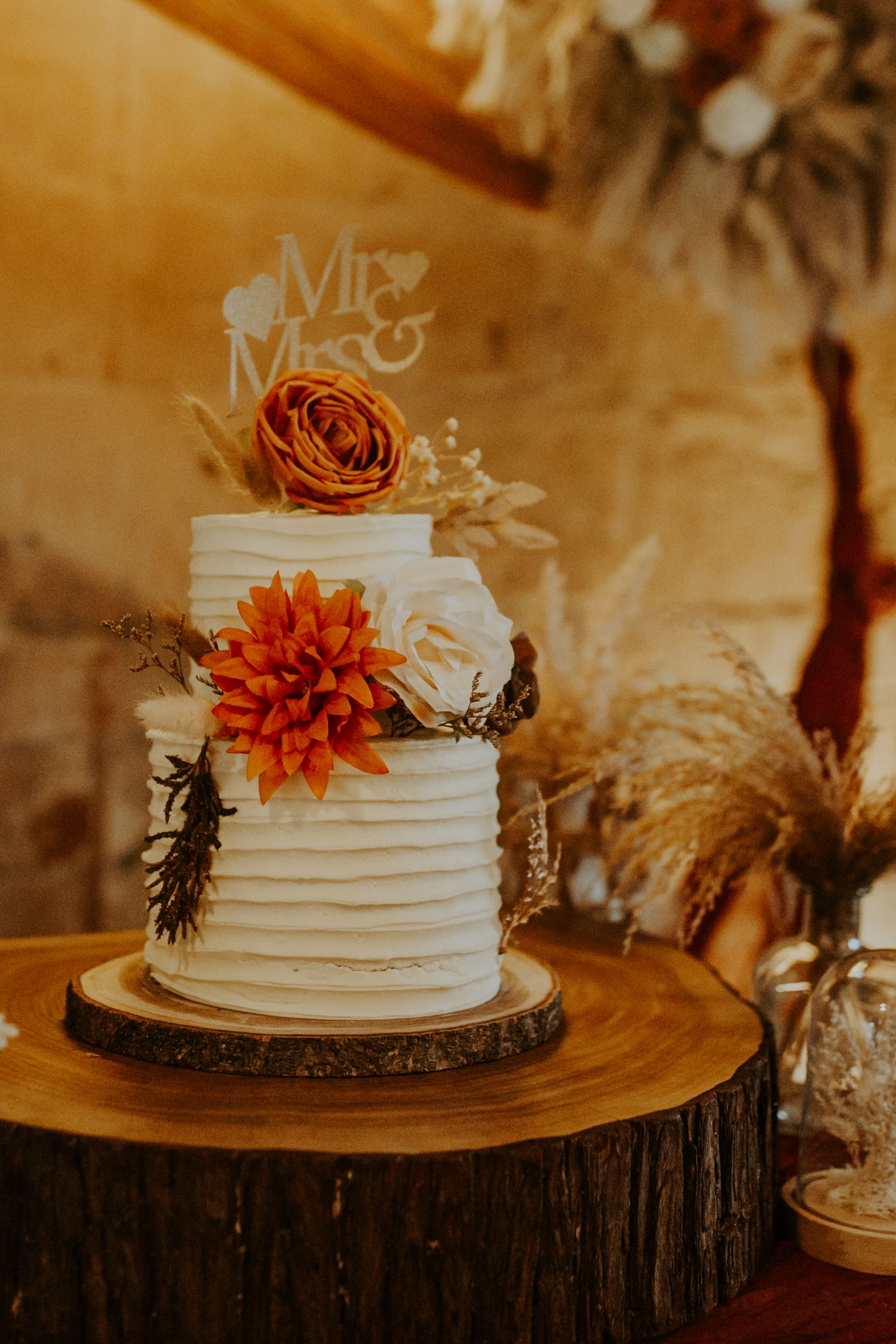 White 2 tier wedding cake with burnt orange flowers at wedding reception at Lapstone Barn – Chipping Campden, The Cotswolds