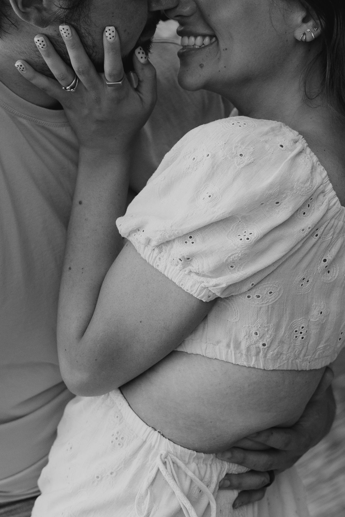 Black and white photo of a pregnant couple sharing an intimate moment, woman in white eyelet crop top.
