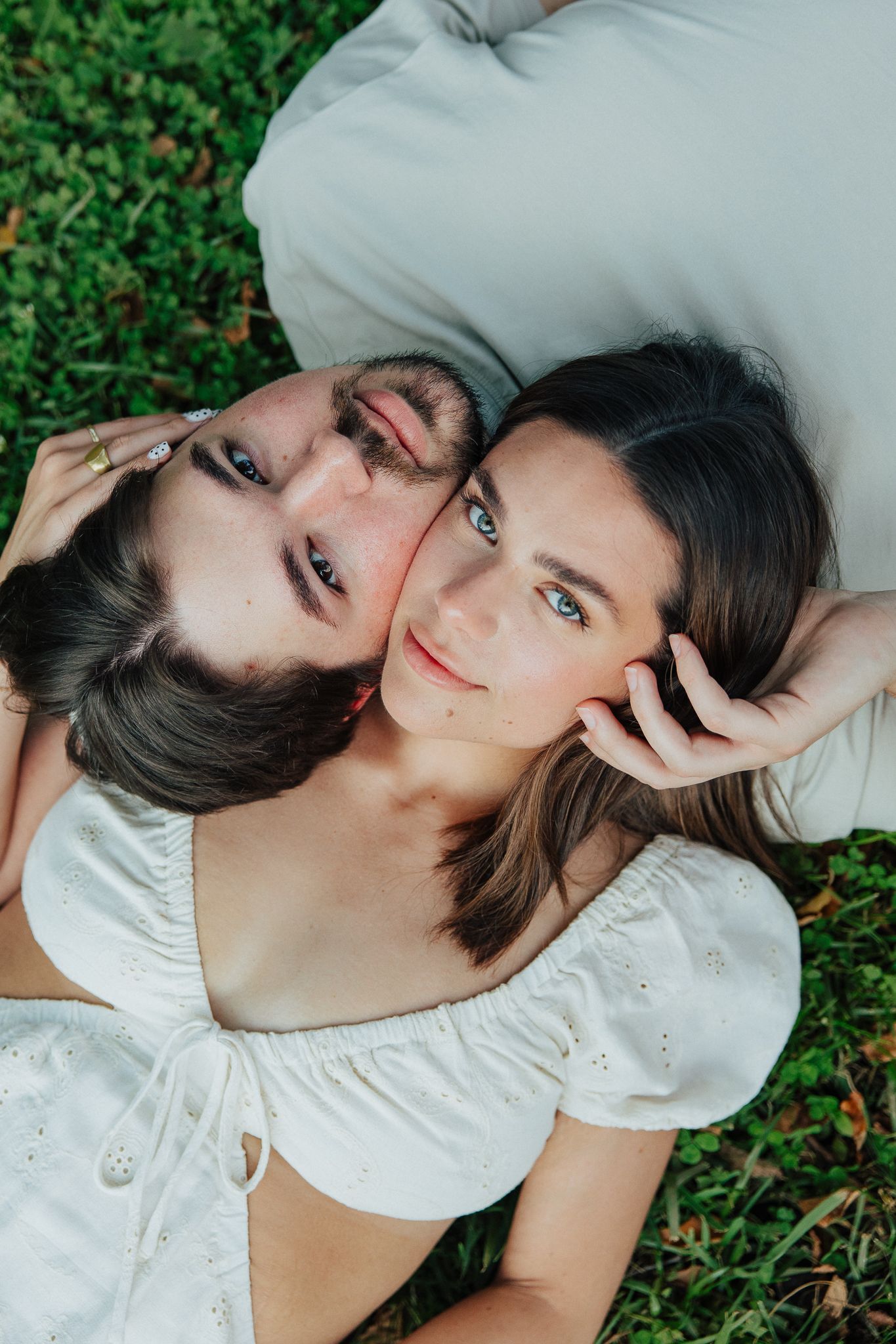 Overhead view of couple lying on green grass, looking up at camera in a romantic pose.