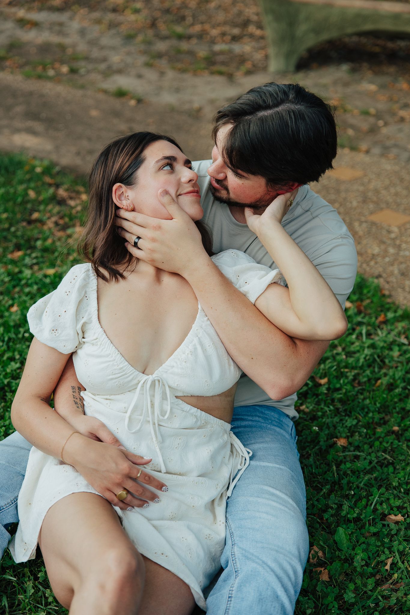 Couple sitting on grass, man tenderly holding womans face as they gaze at each other.
