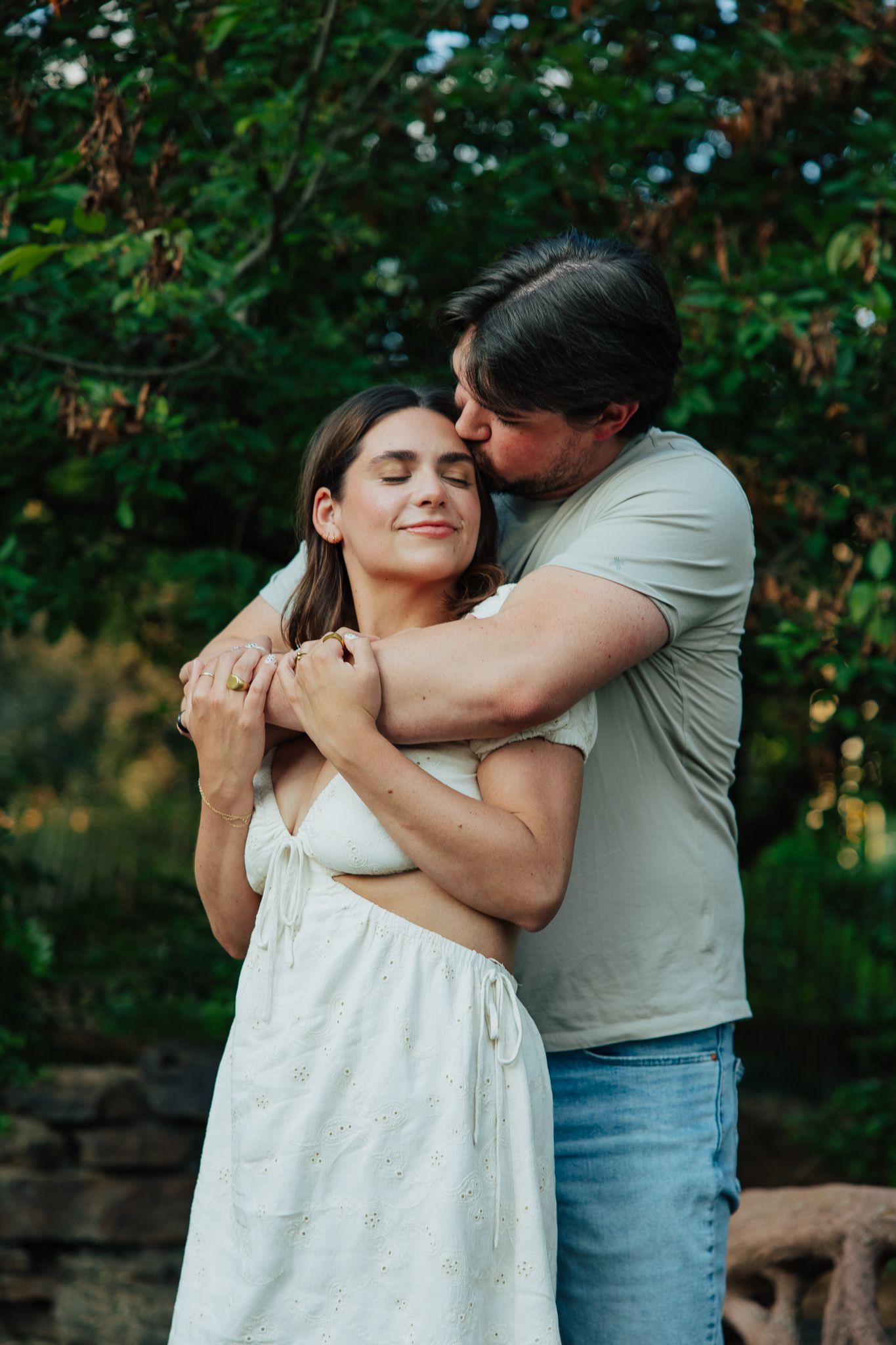 Man tenderly embracing woman from behind during romantic outdoor engagement photo session.