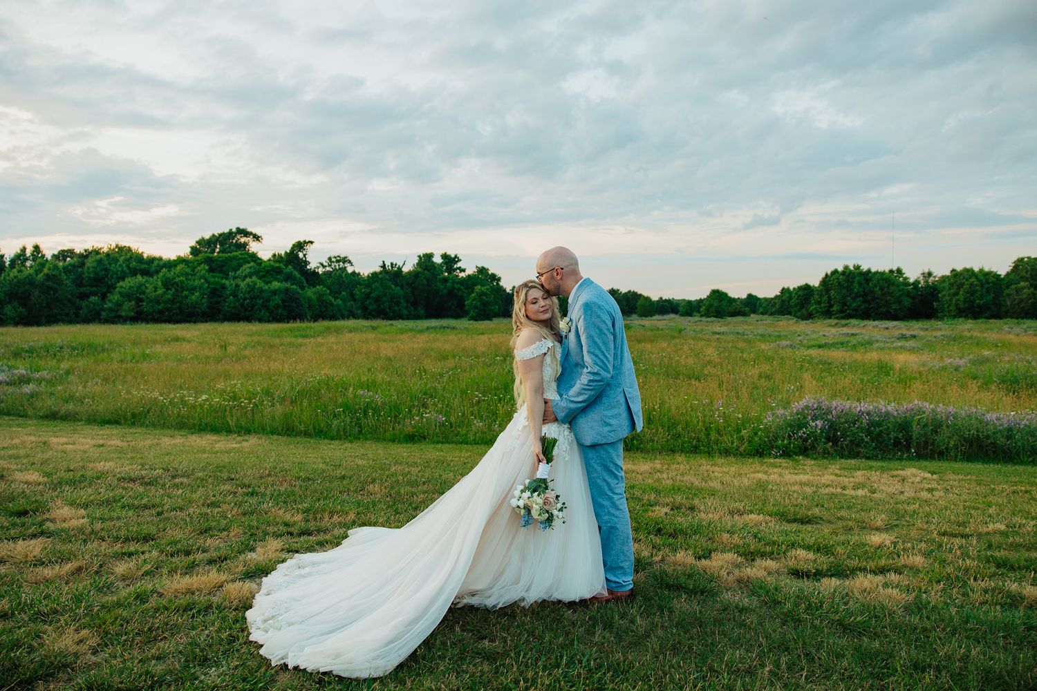 Newlywed couple embracing in lush green field during golden hour wedding photography.