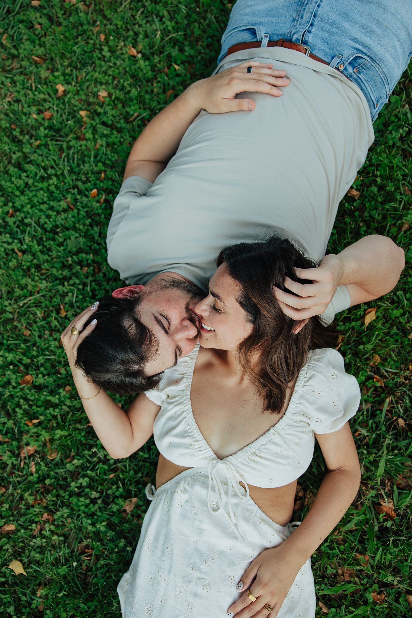 Aerial view of couple lying on green grass, sharing a tender kiss in a romantic outdoor setting.