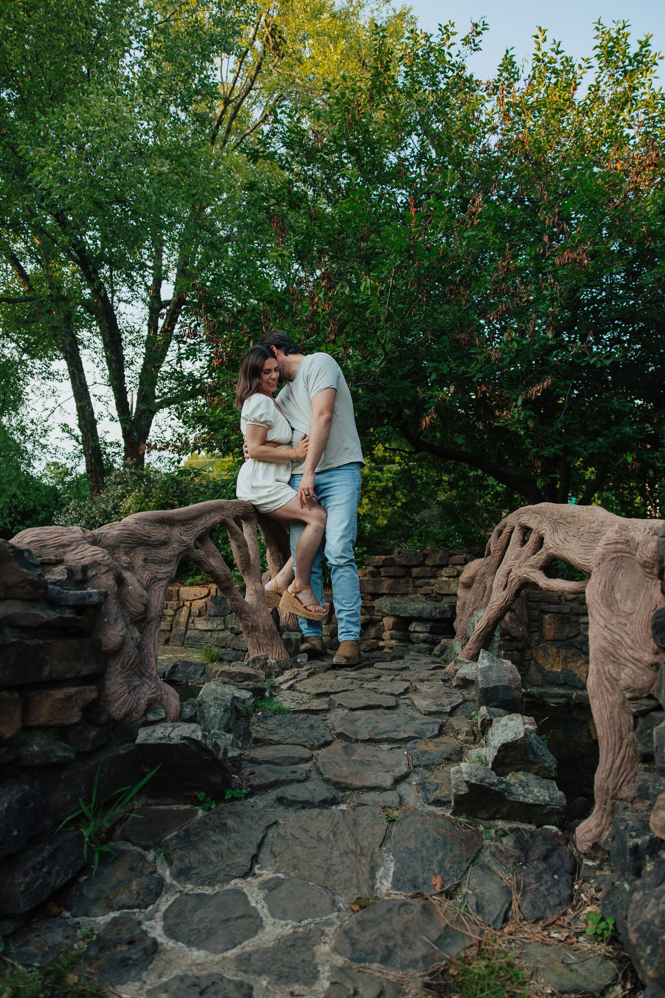Couple sharing intimate moment seated on rustic stone bridge in lush garden setting.