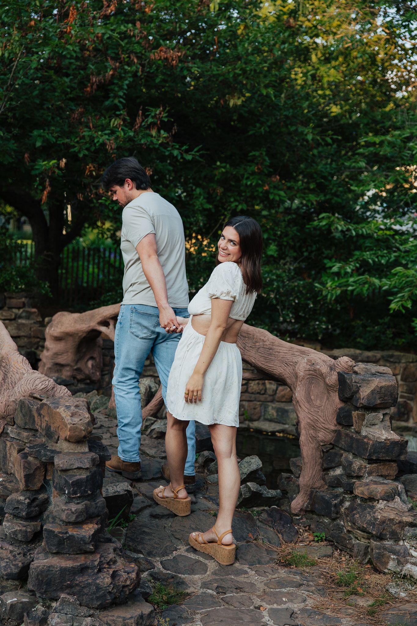 Woman smiling back at camera while holding hands with partner on stone bridge.